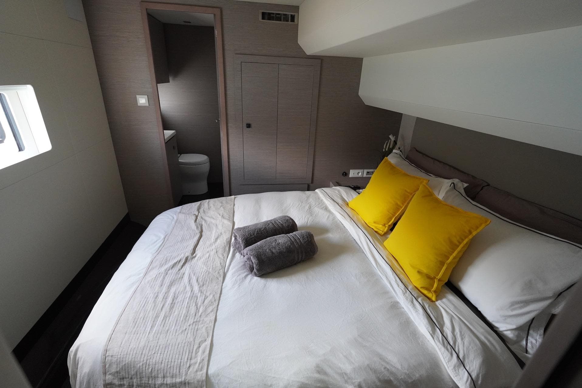 Luxurious bedroom in 2023 Fountaine Pajot MY6 yacht with yellow pillows and ensuite bathroom.