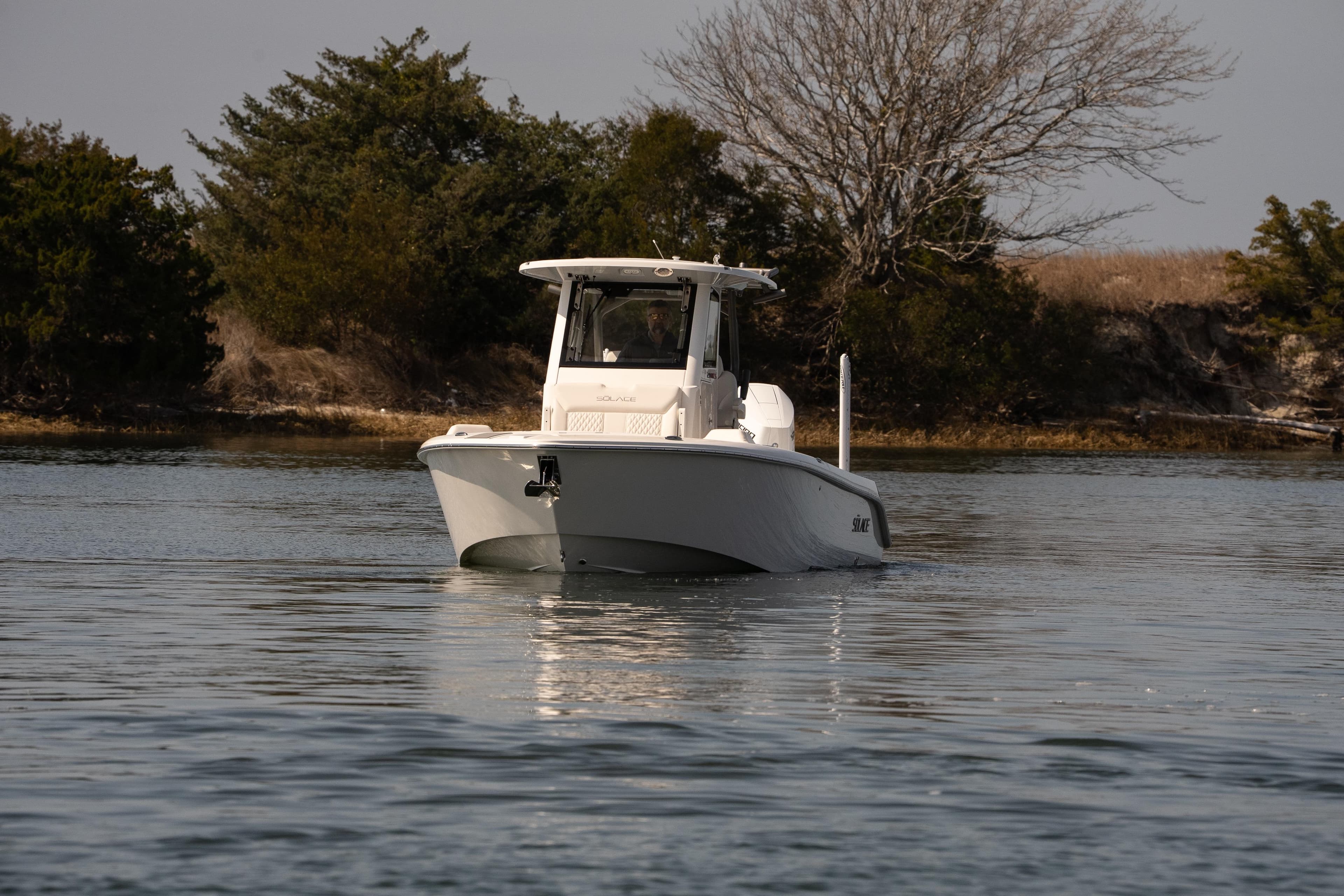 2026 Solace 28 HCS boat cruising on calm water near a wooded shoreline.