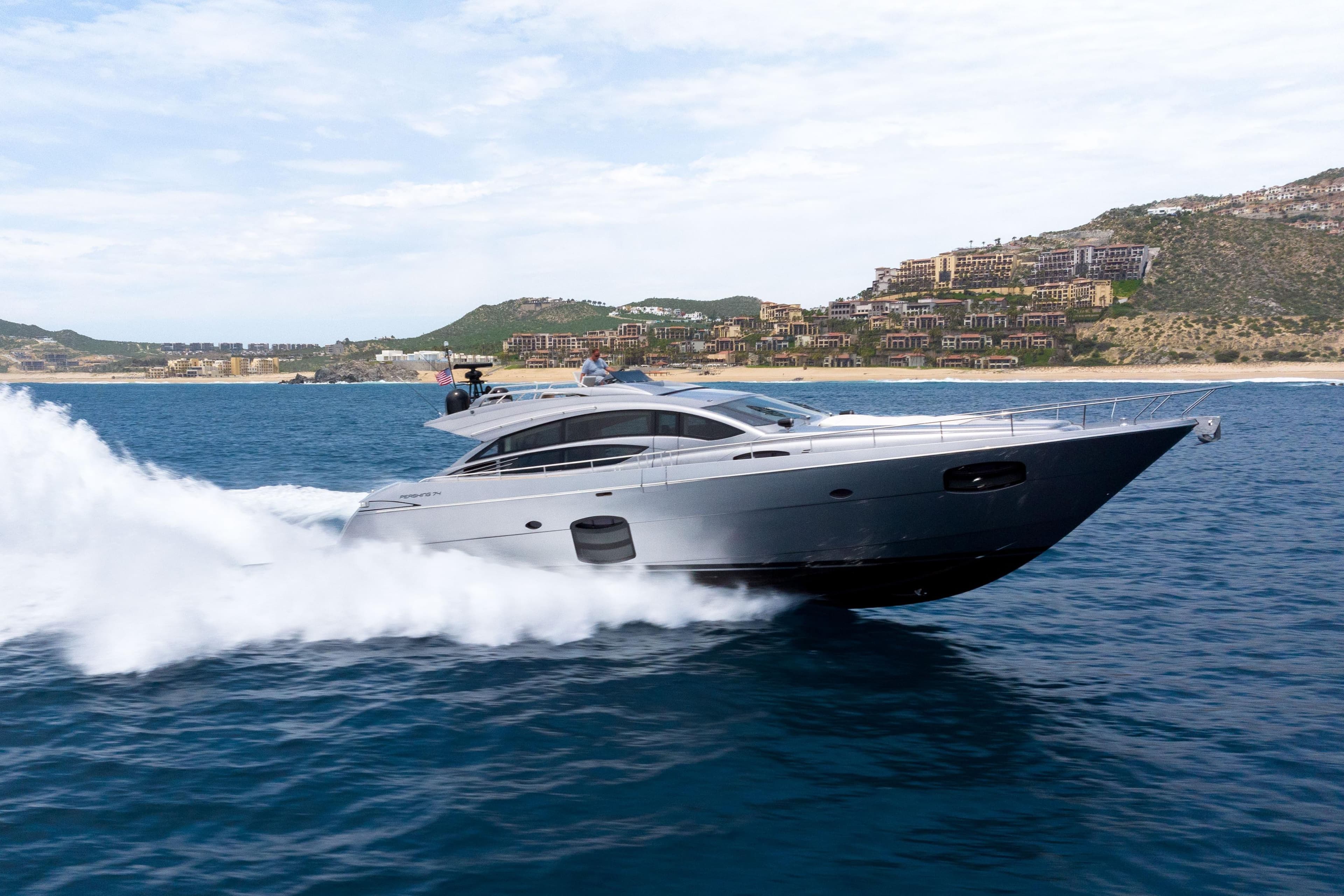 2017 Pershing 74 yacht cruising on ocean near coastal landscape.