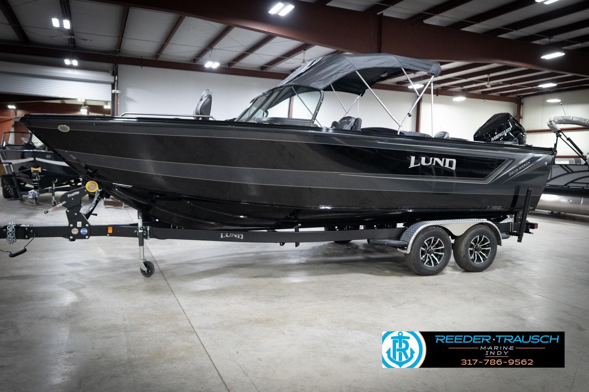 2026 Lund 2275 Baron boat on trailer in indoor showroom, featuring sleek black design.