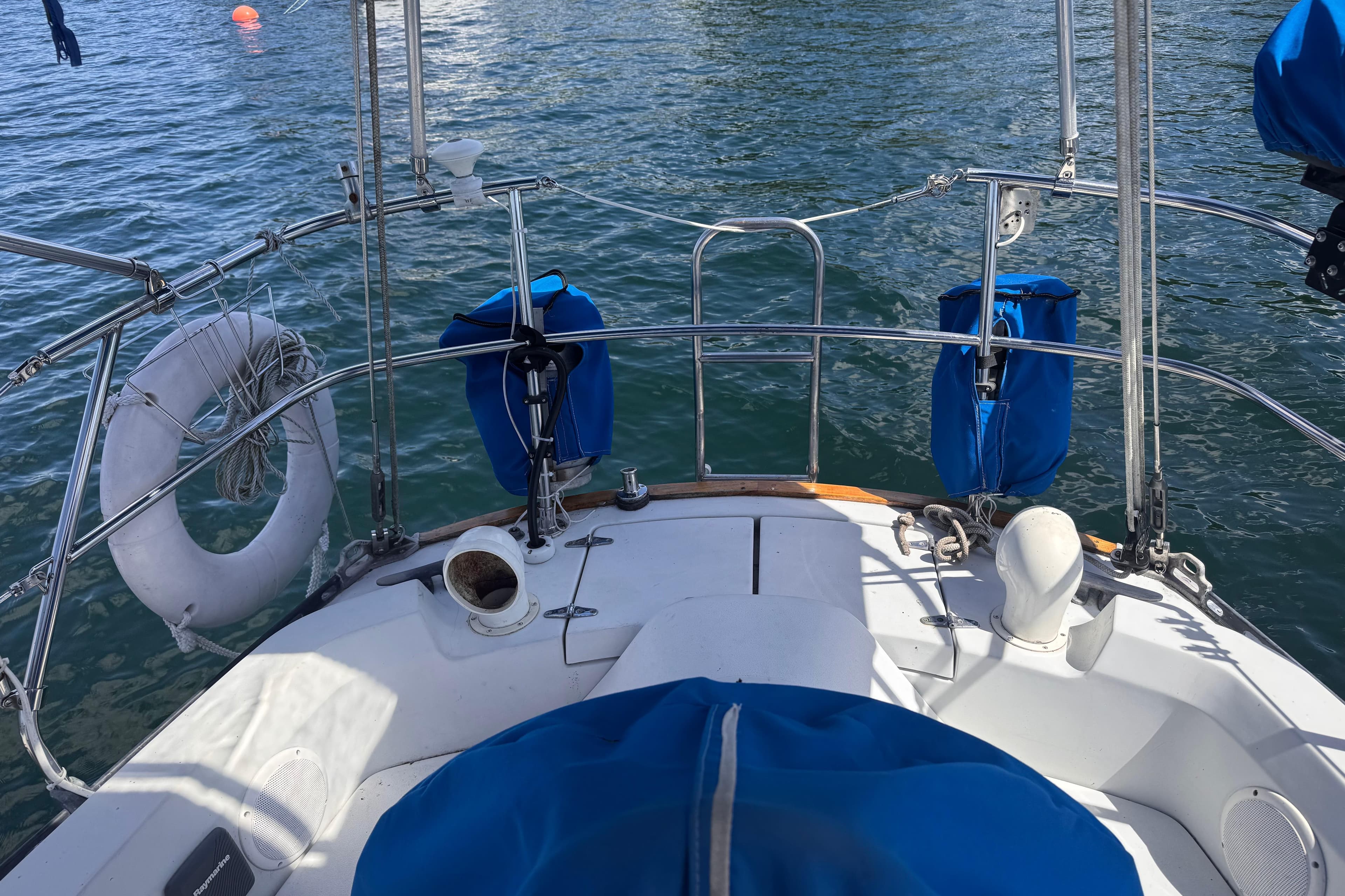 1983 C&C 32 sailboat deck with life ring and blue covers on calm water.