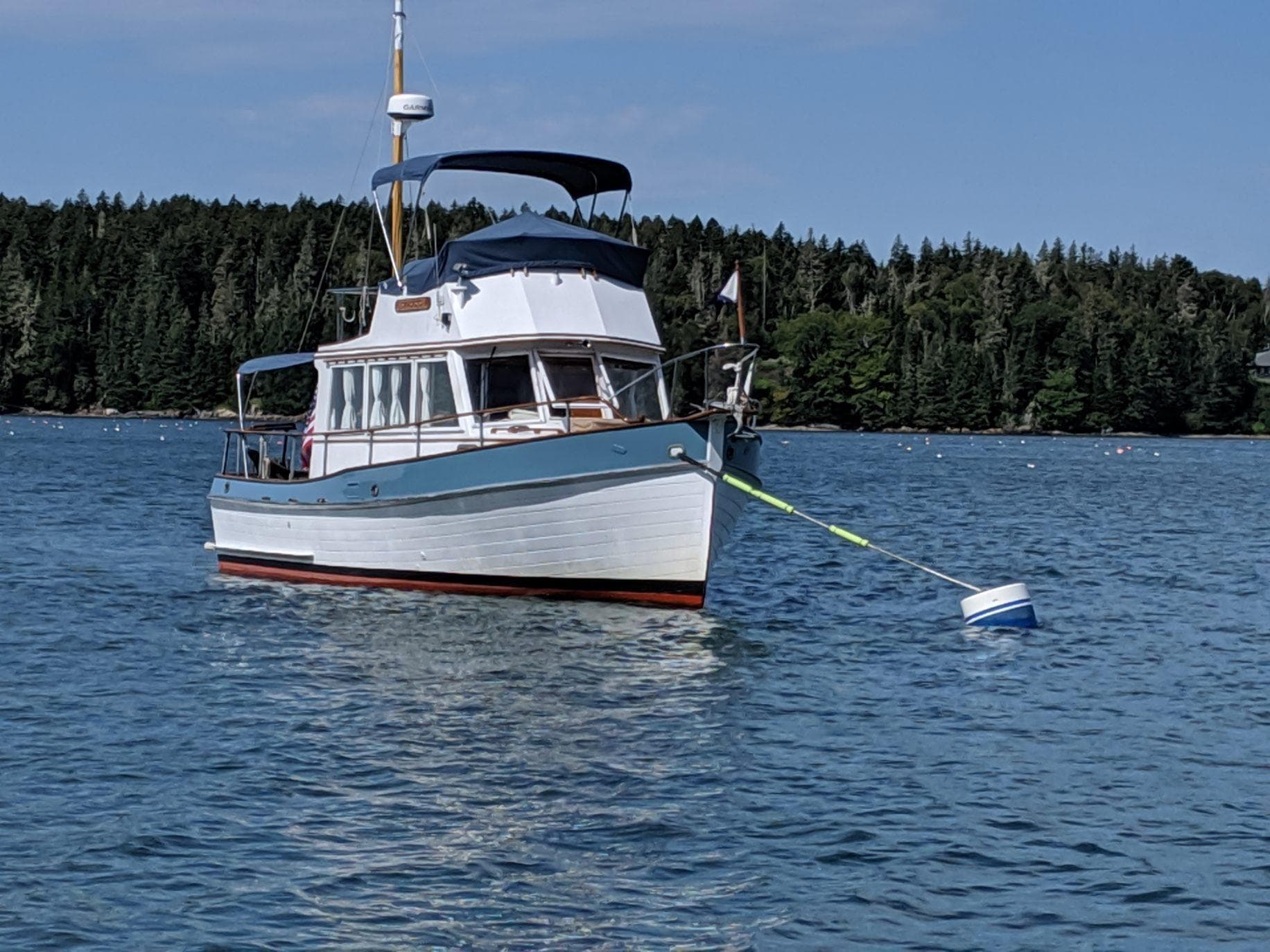 1972 Grand Banks Trawler anchored on calm water with forested shoreline in the background.
