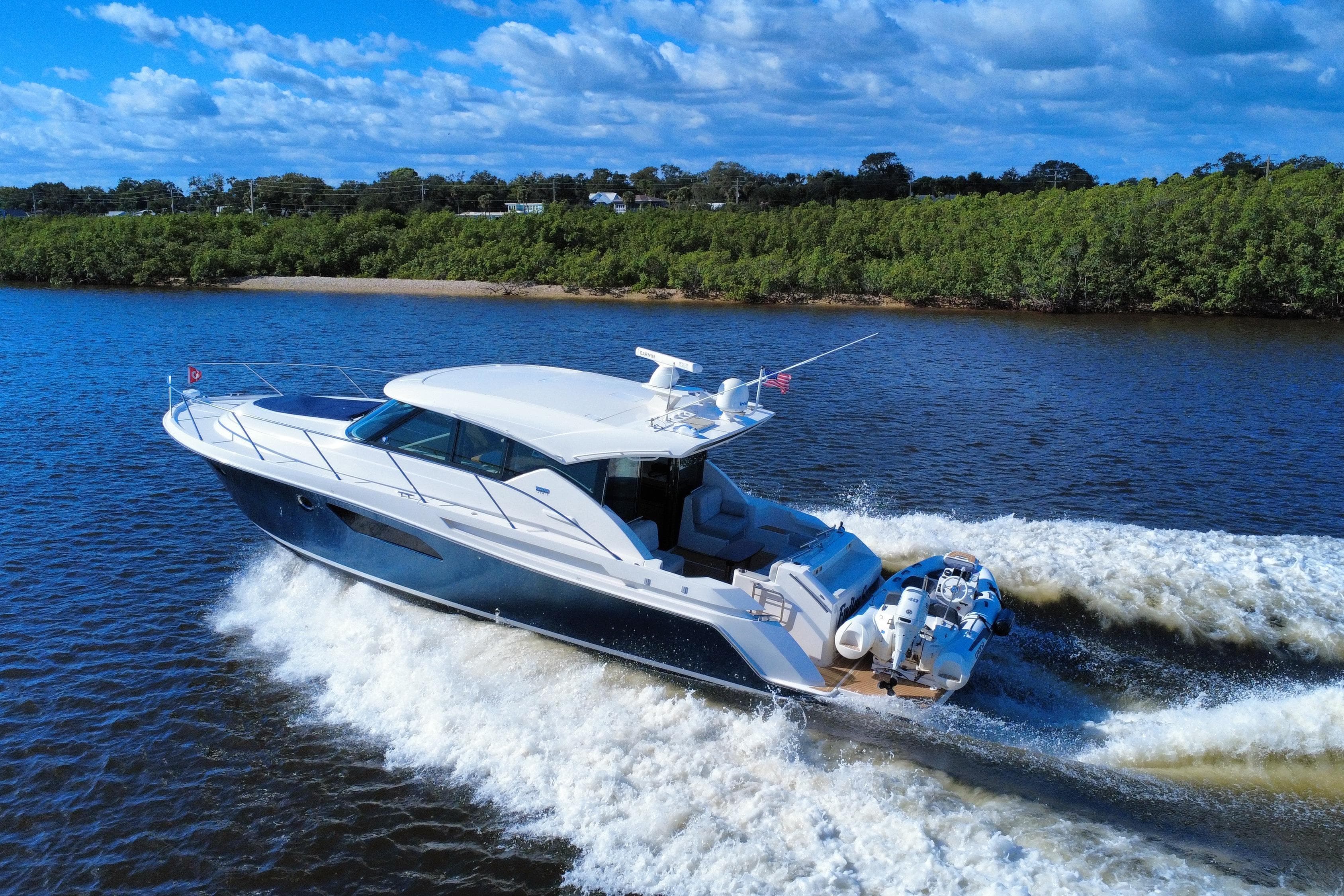 2016 Tiara Yachts C44 Coupe cruising on a scenic river under a blue sky.