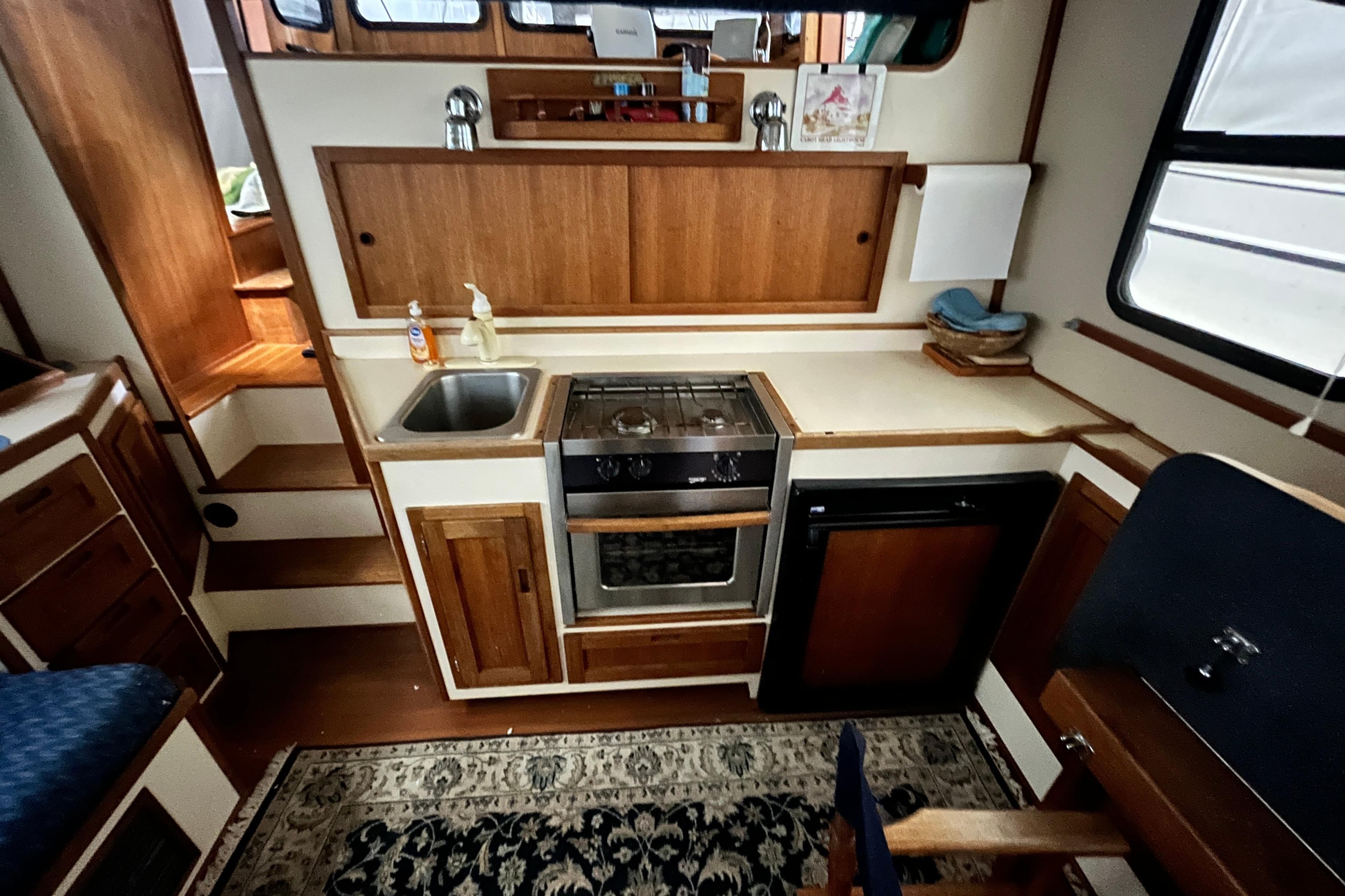 1999 Nordic Tug 32 interior kitchen with wooden cabinetry, sink, stove, and compact refrigerator.