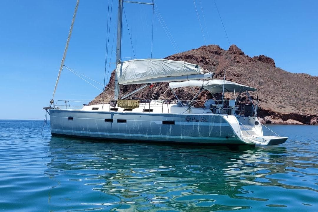 Sailing yacht Bavaria 45, 2011 model, anchored in clear blue waters near rocky coastline.