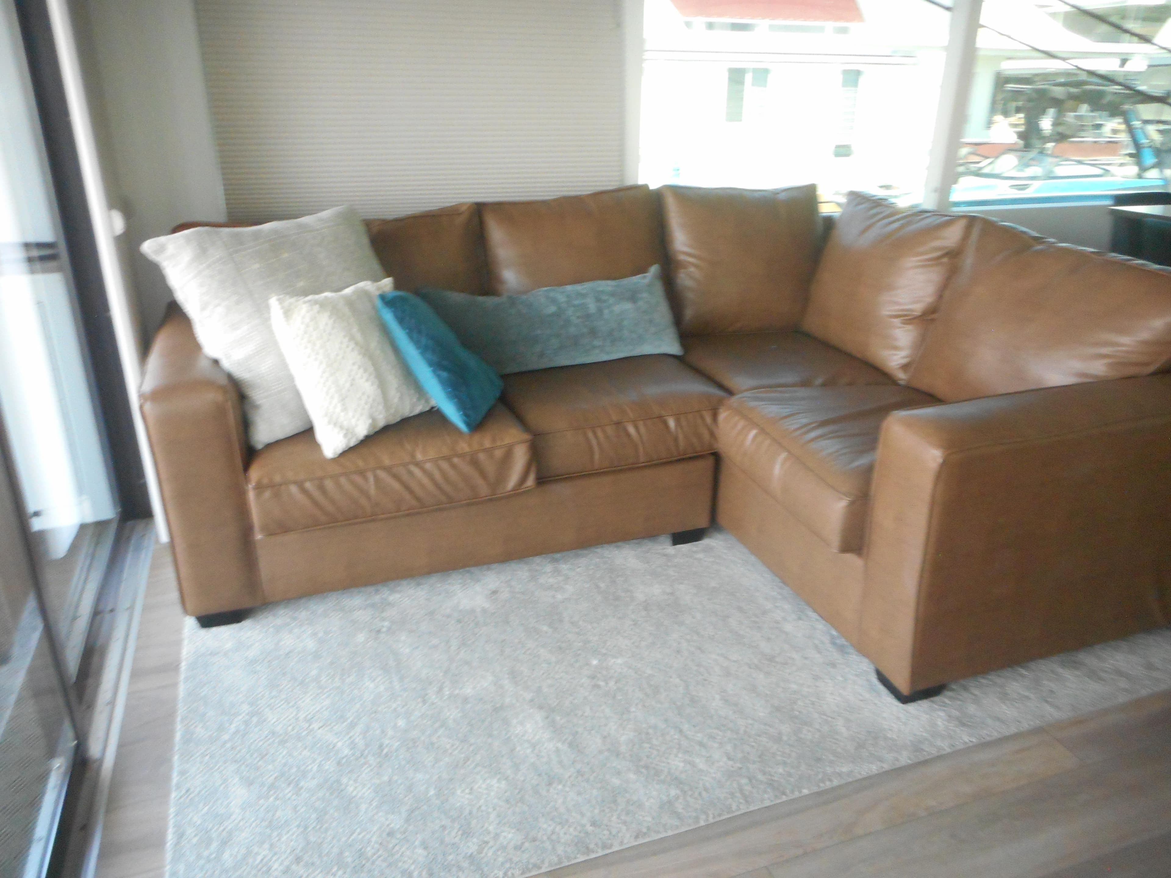 Brown leather sectional sofa with assorted pillows on a light rug, Adonia Obsession Trip #12, 2021.