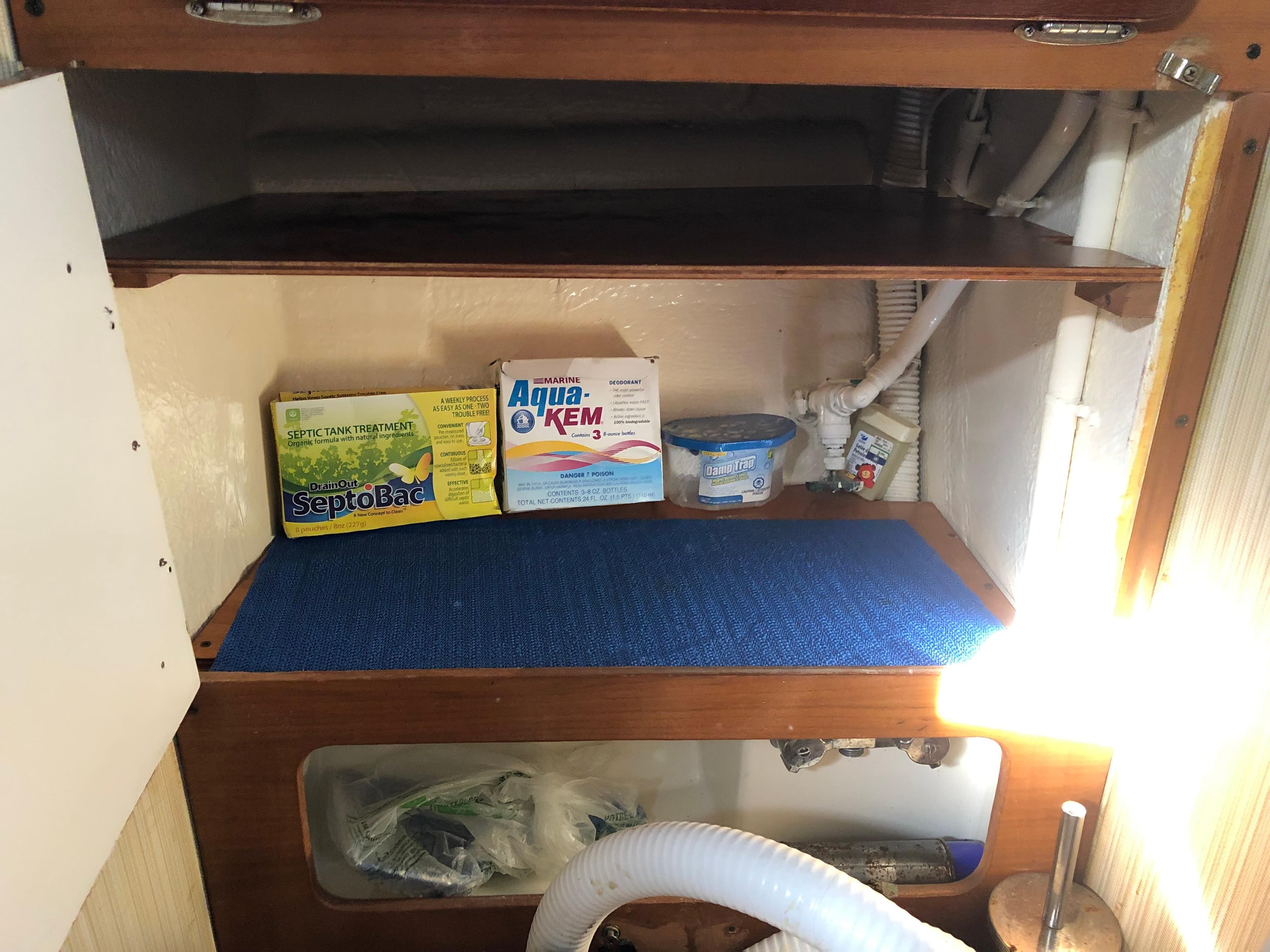 1980 Pearson 323 boat interior storage with cleaning supplies and blue mat.