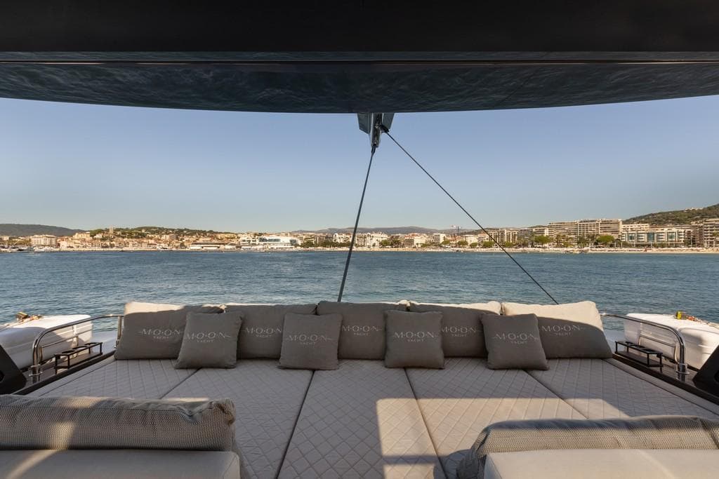 Luxurious Moon 60 Sail yacht deck with cushions, overlooking serene coastal cityscape, 2026 model.