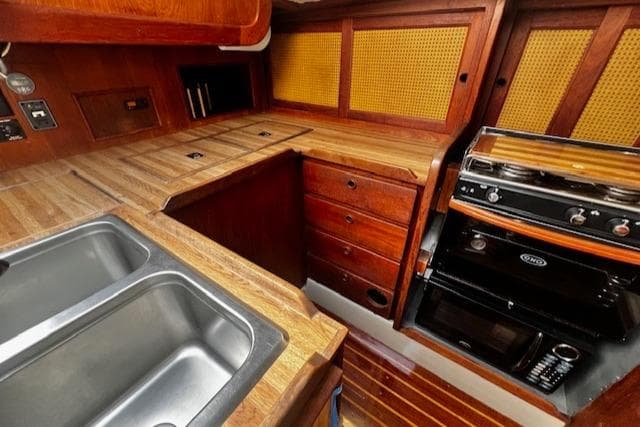 1980 CAL 39 MK II Sloop interior kitchen with wooden cabinetry, sink, and stove.