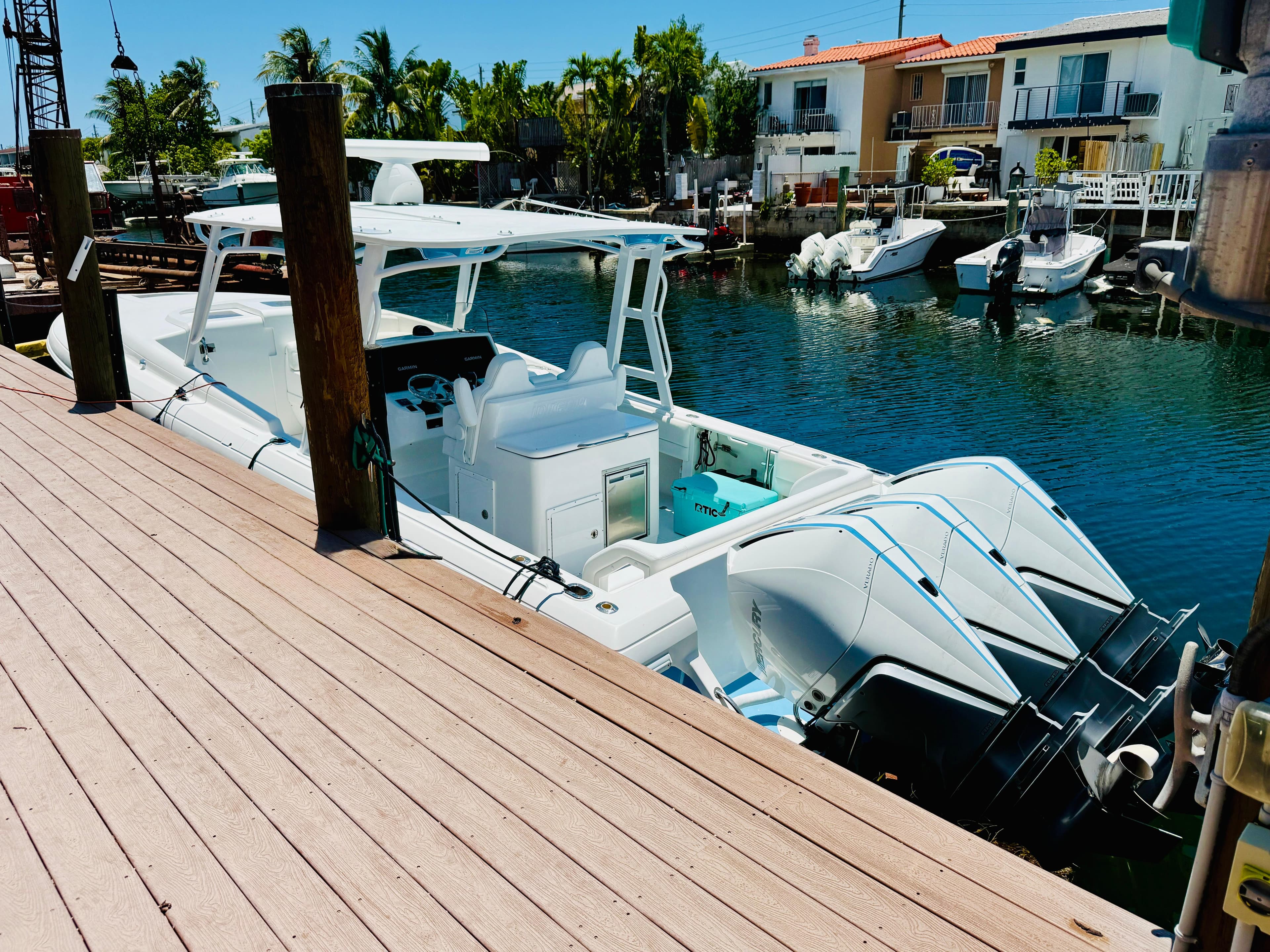 2003 Intrepid 377 boat docked by waterfront homes, featuring triple outboard engines.