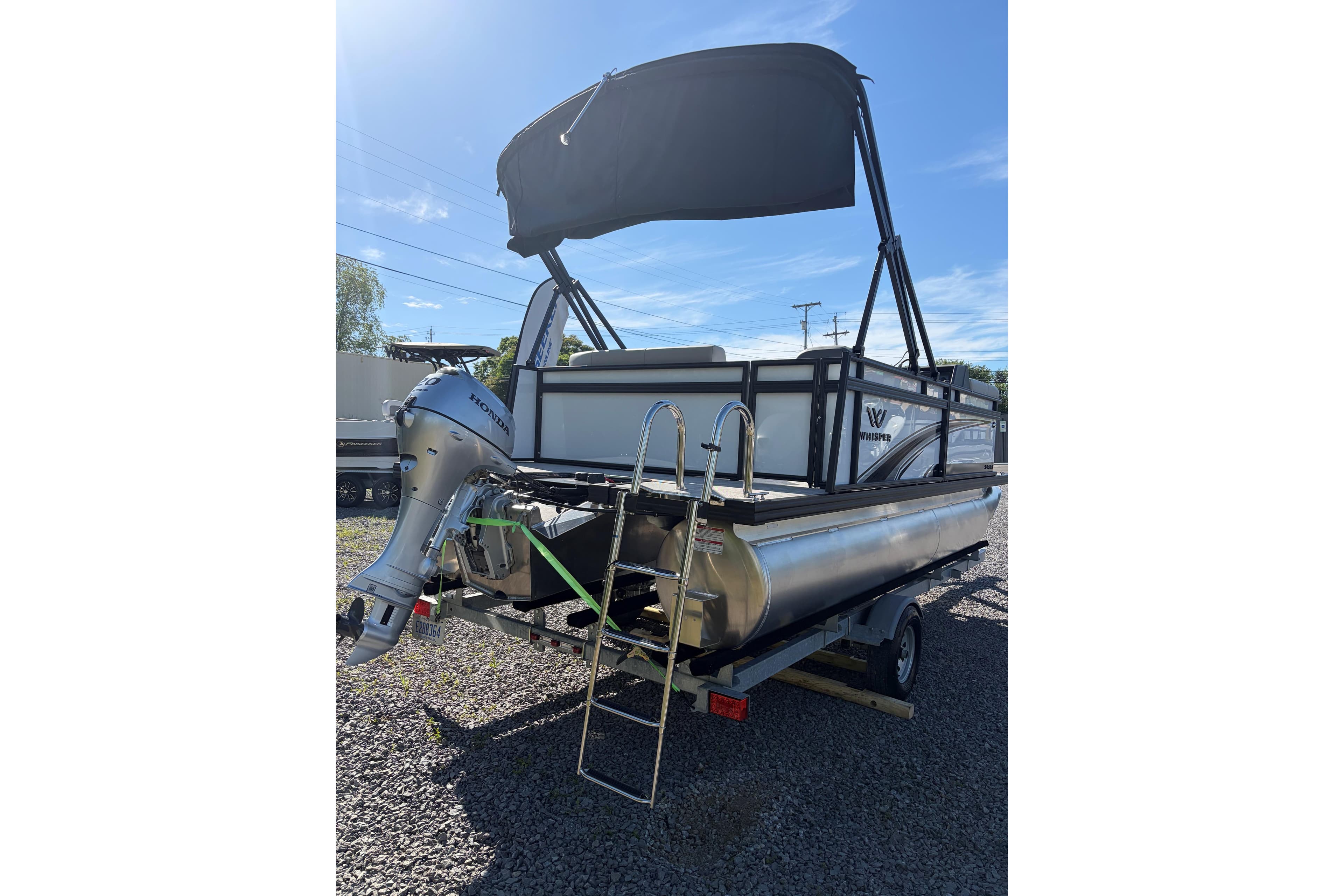 Pontoon boat Whisper S17 2026 with outboard motor and canopy on gravel.