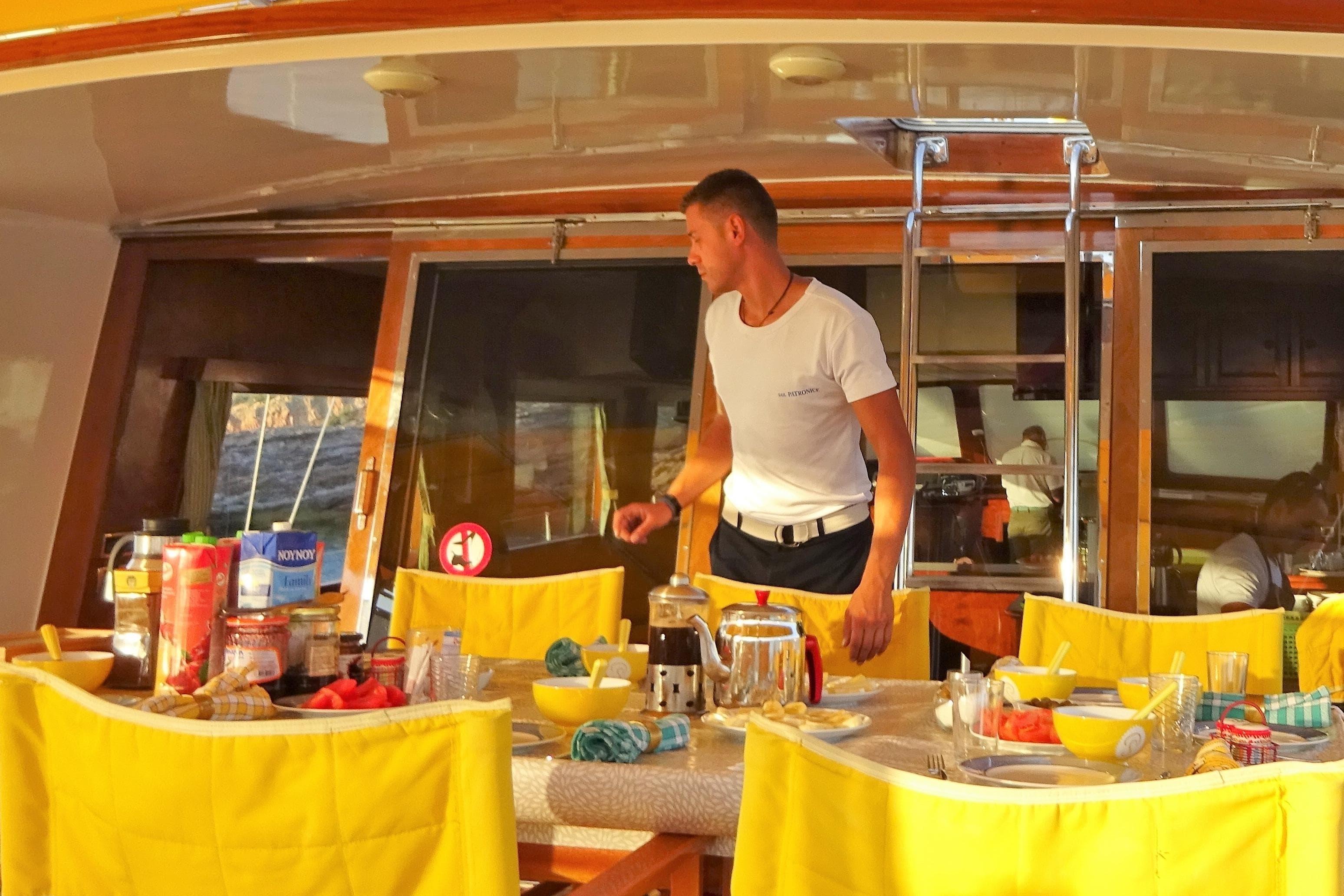Man preparing breakfast on a 1992 Baymarin Custom yacht with yellow chairs.