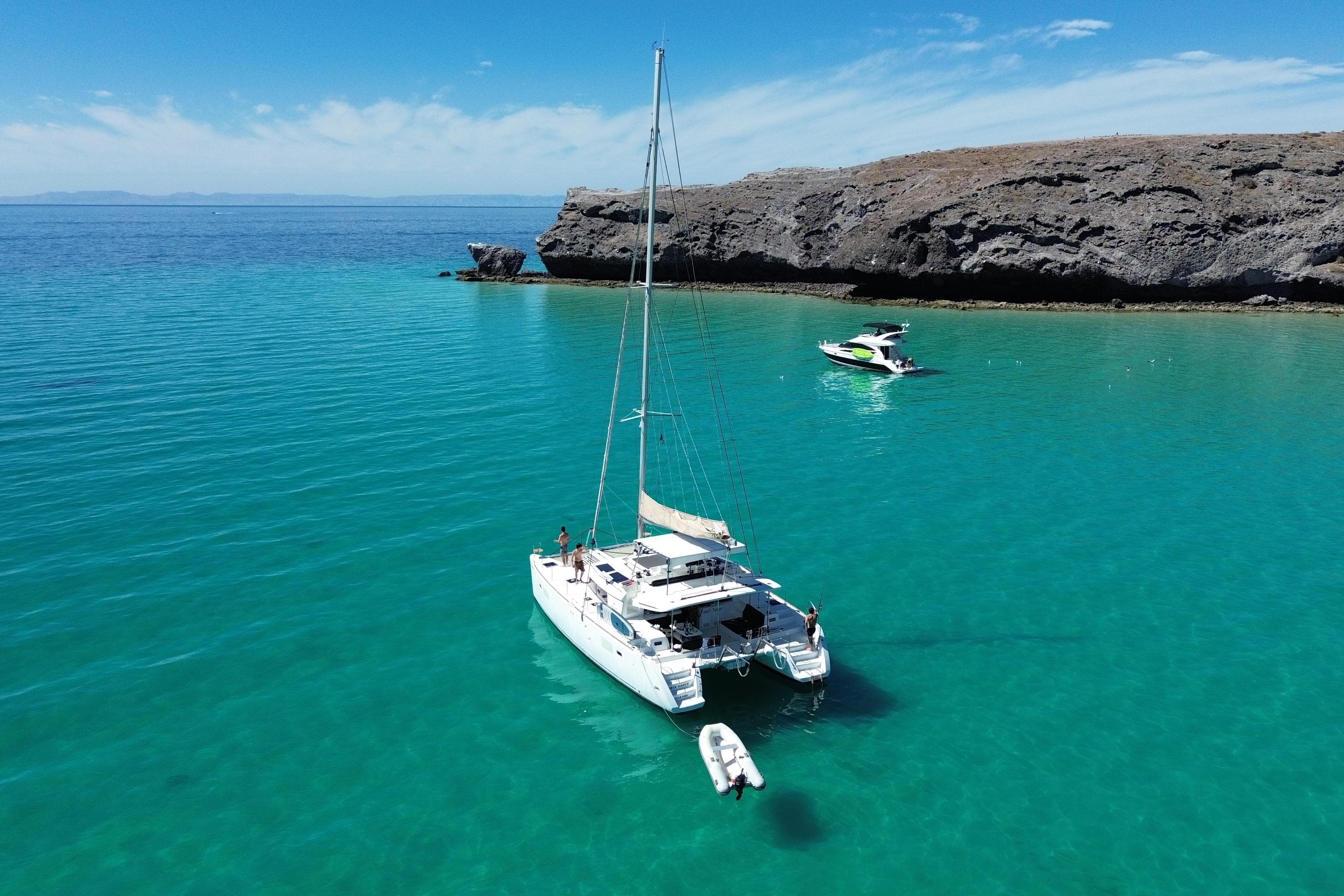 2019 Lagoon 450 F catamaran anchored in clear turquoise waters near rocky coastline.