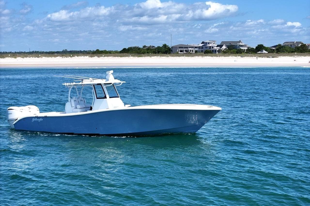 2026 Yellowfin 36 Offshore boat cruising near a sandy beach under a blue sky.