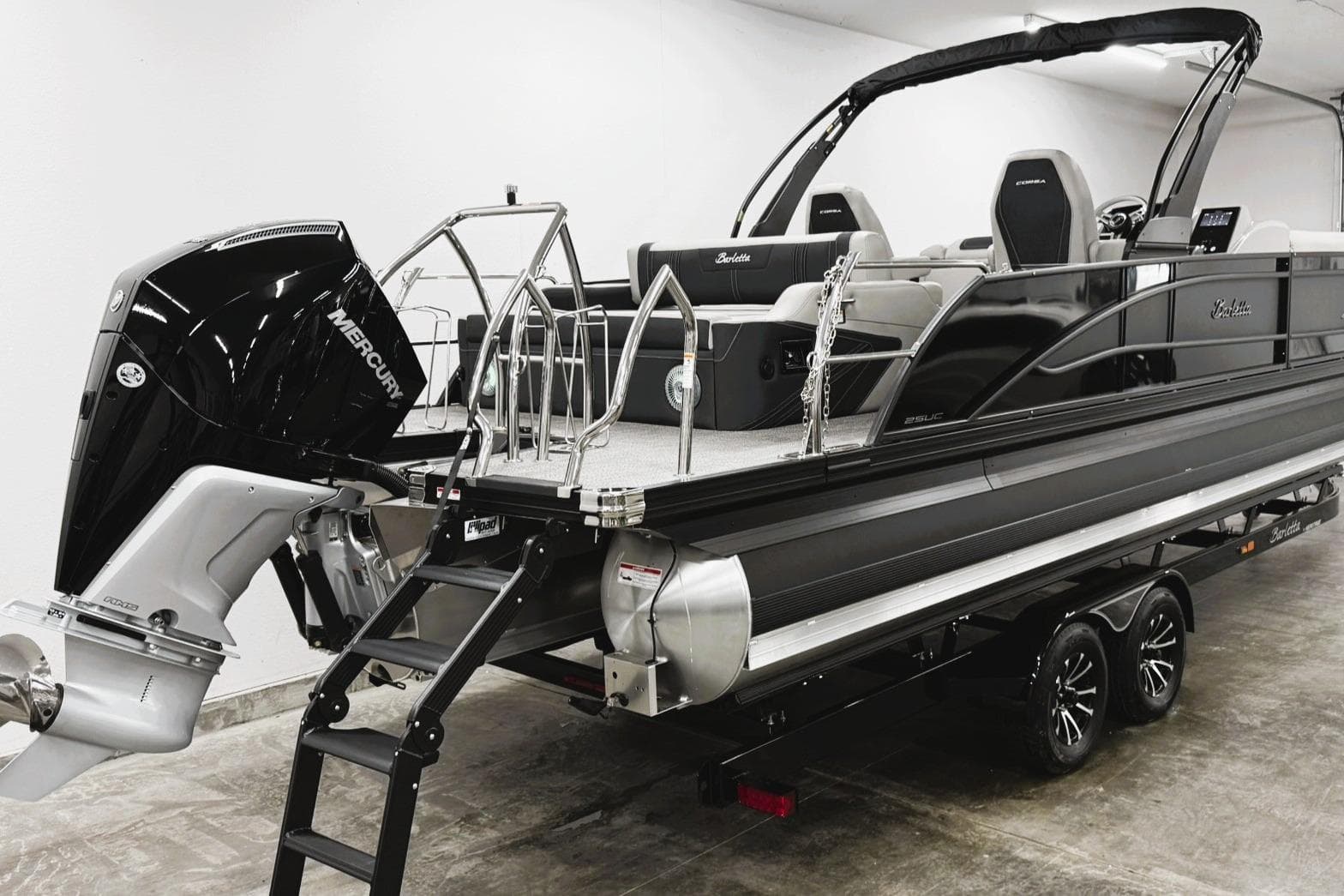 2026 Barletta CORSA 25UC pontoon boat with Mercury engine, displayed indoors on a trailer.
