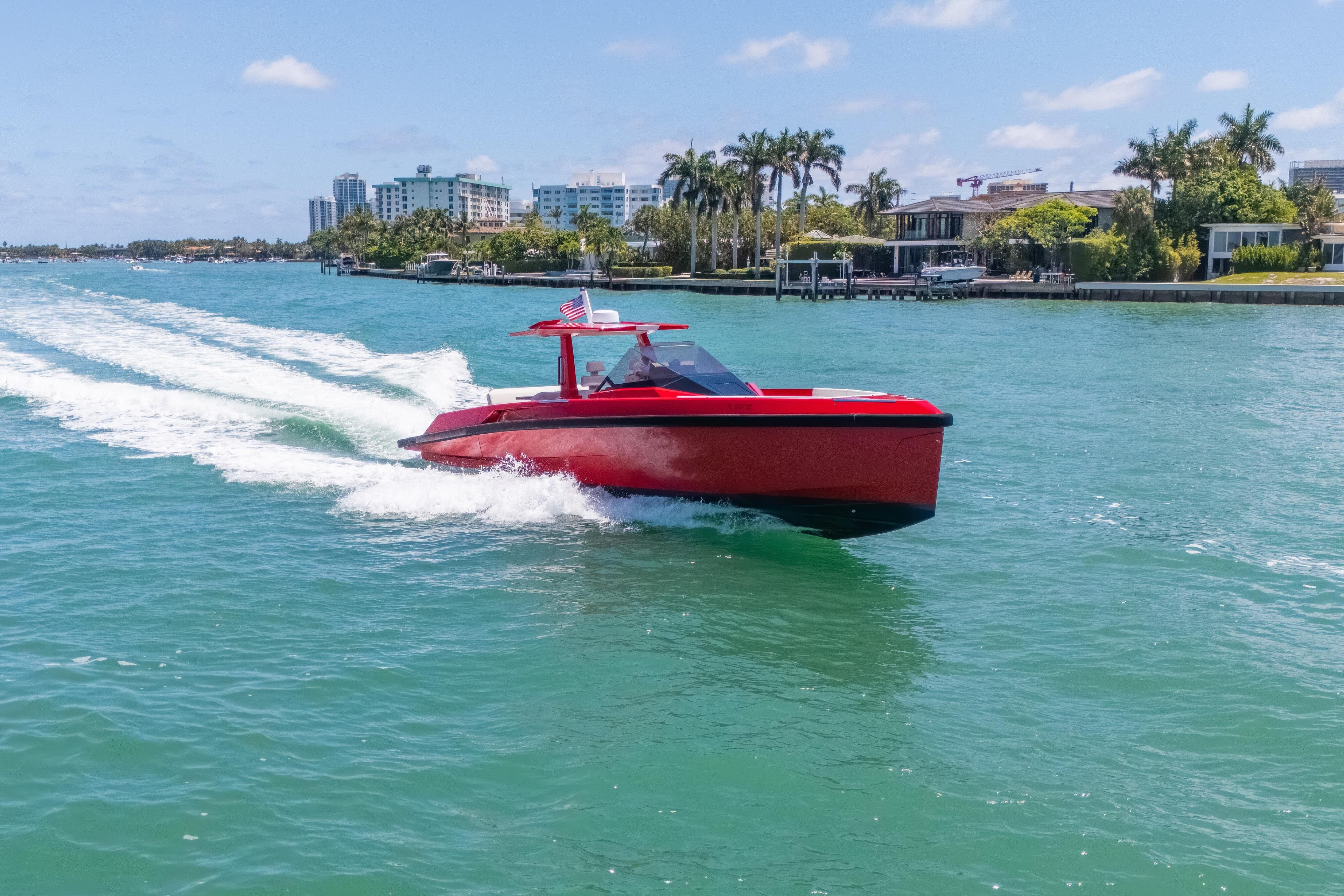 Red 2021 Wally 48 yacht cruising on turquoise water near a coastal cityscape.