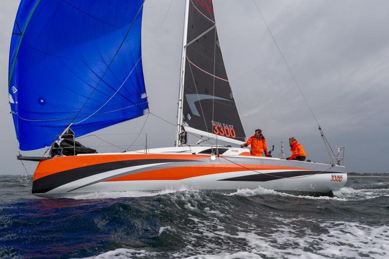 2025 Jeanneau Sun Fast 3300 sailing with vibrant blue and orange sails on open water.
