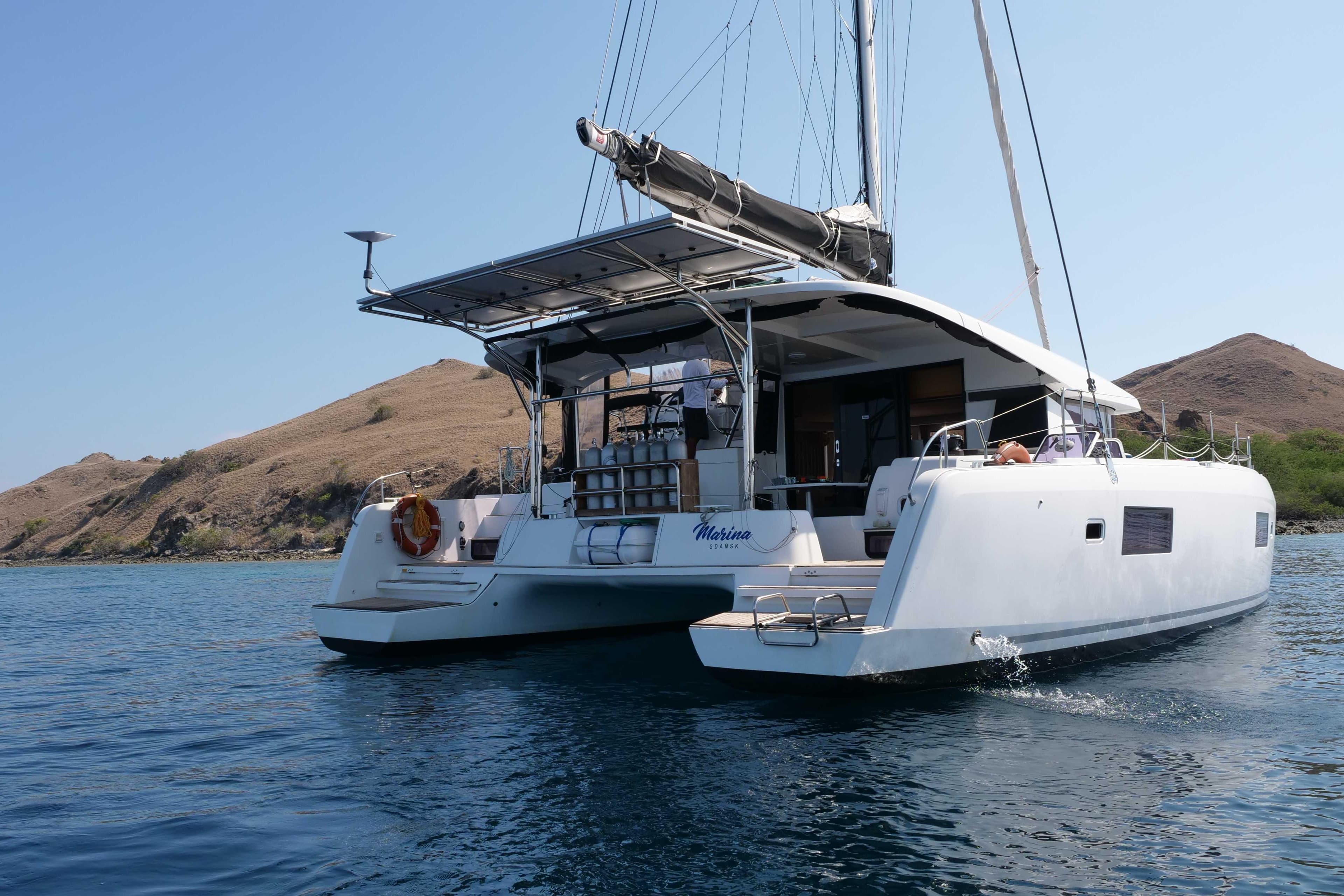 2018 Lagoon 42 catamaran sailing in calm waters near rocky coastline.
