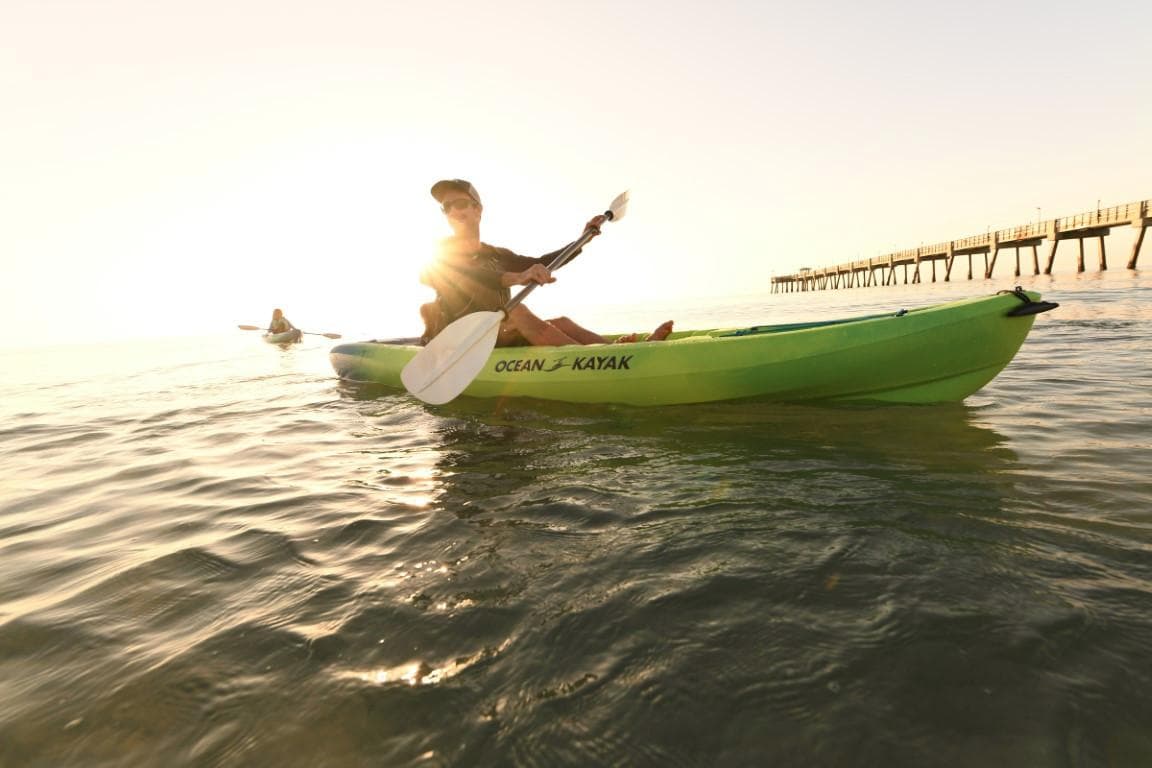 Person kayaking on Ocean Kayak Malibu 9.5 at sunset near a pier, 2023 model.