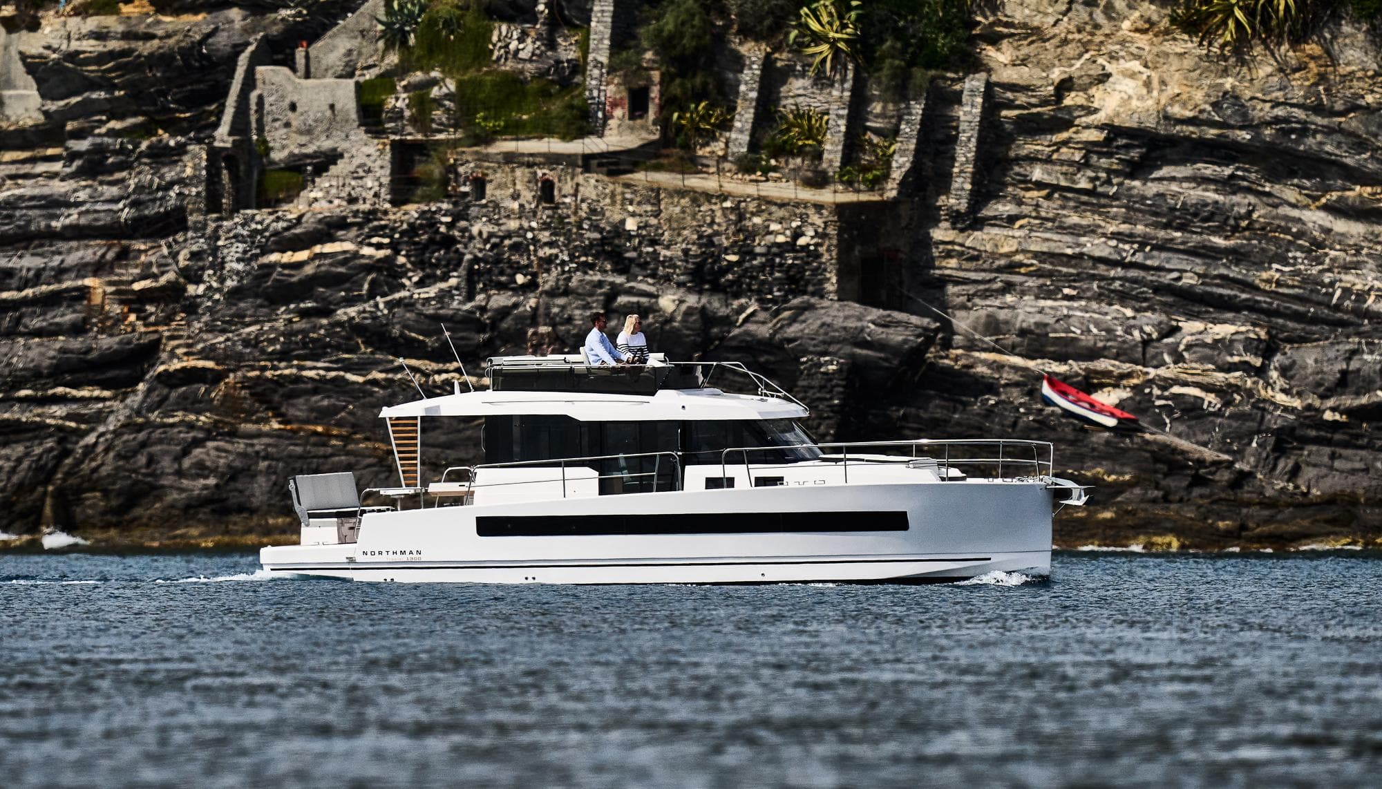 2025 Northman 1300 yacht cruising near rocky shoreline.