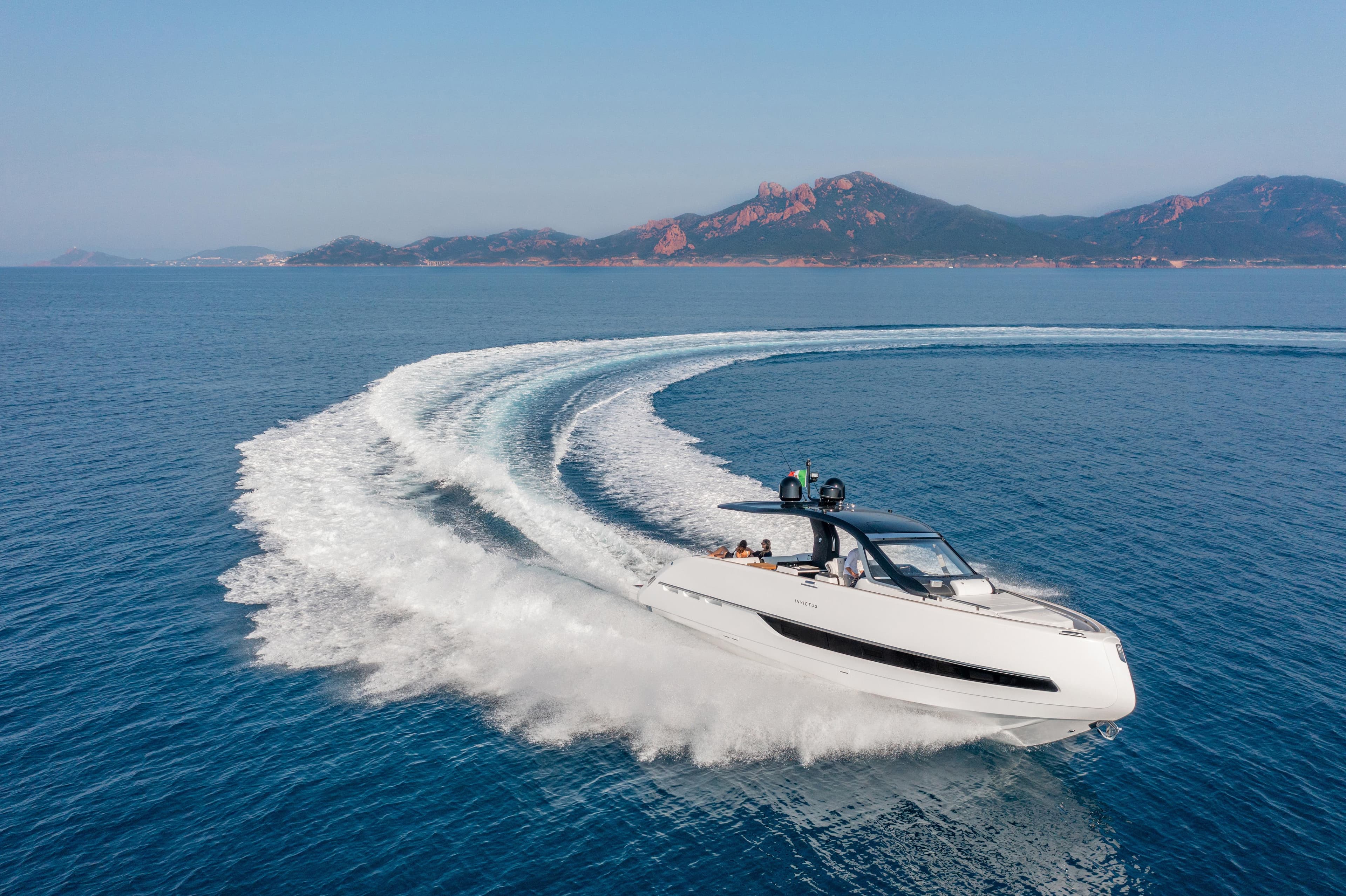 2025 Invictus TT420 yacht cruising on open sea with scenic mountain backdrop.