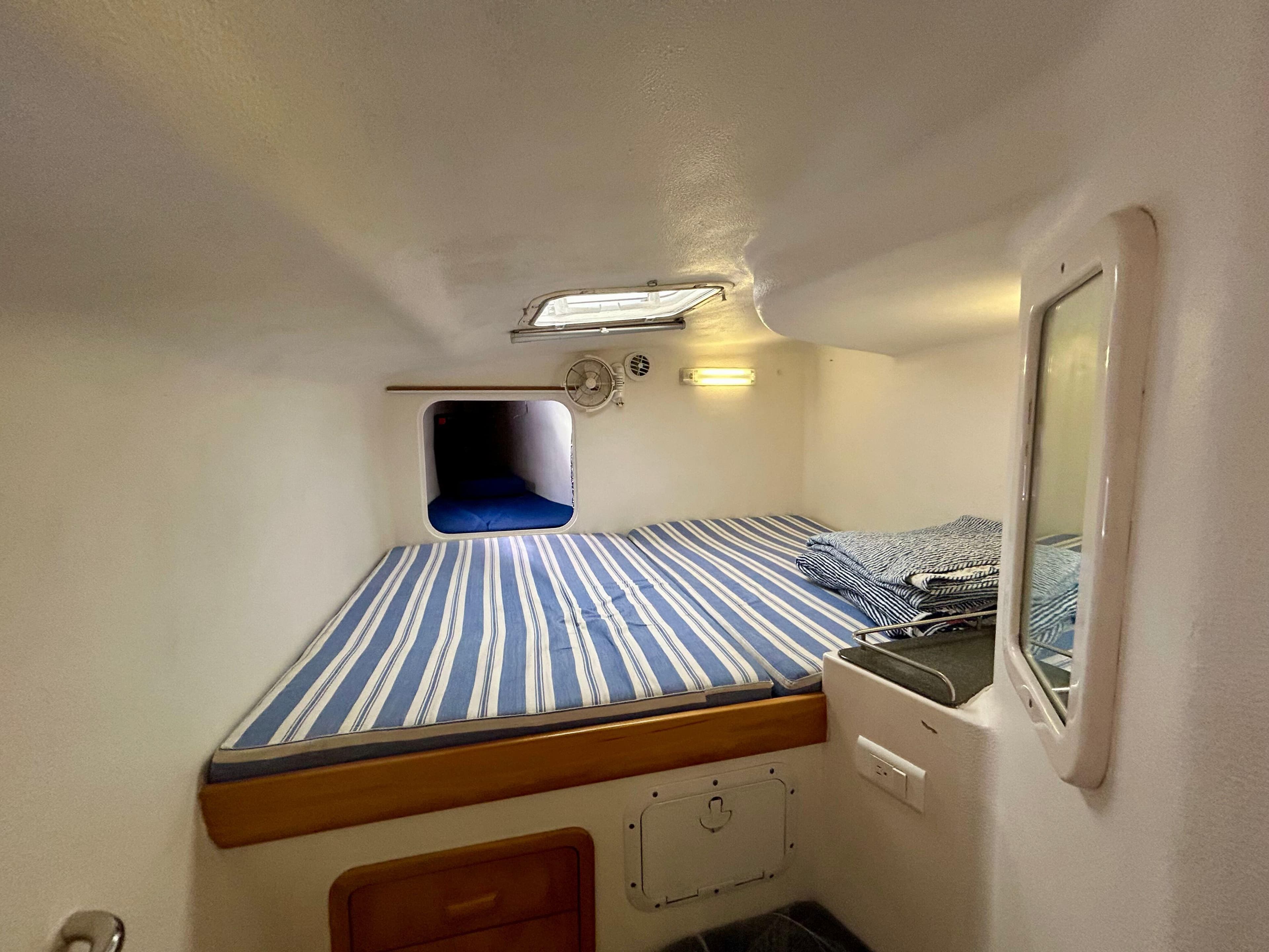 Compact cabin interior of 2001 Voyage Maxim with striped bedding and small window.