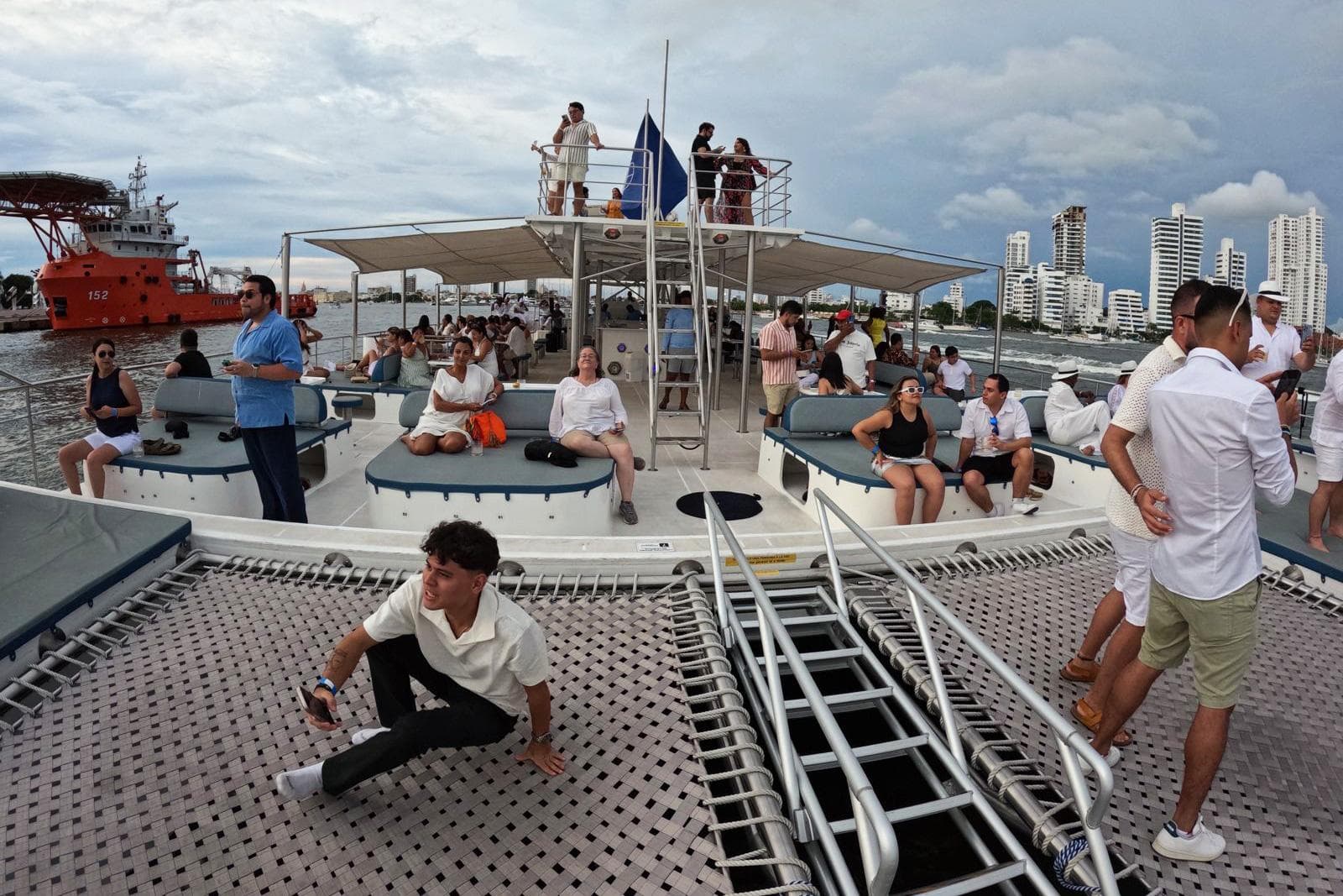 People relaxing on a Custom PaxCat 80 catamaran, 2024, with city skyline in background.