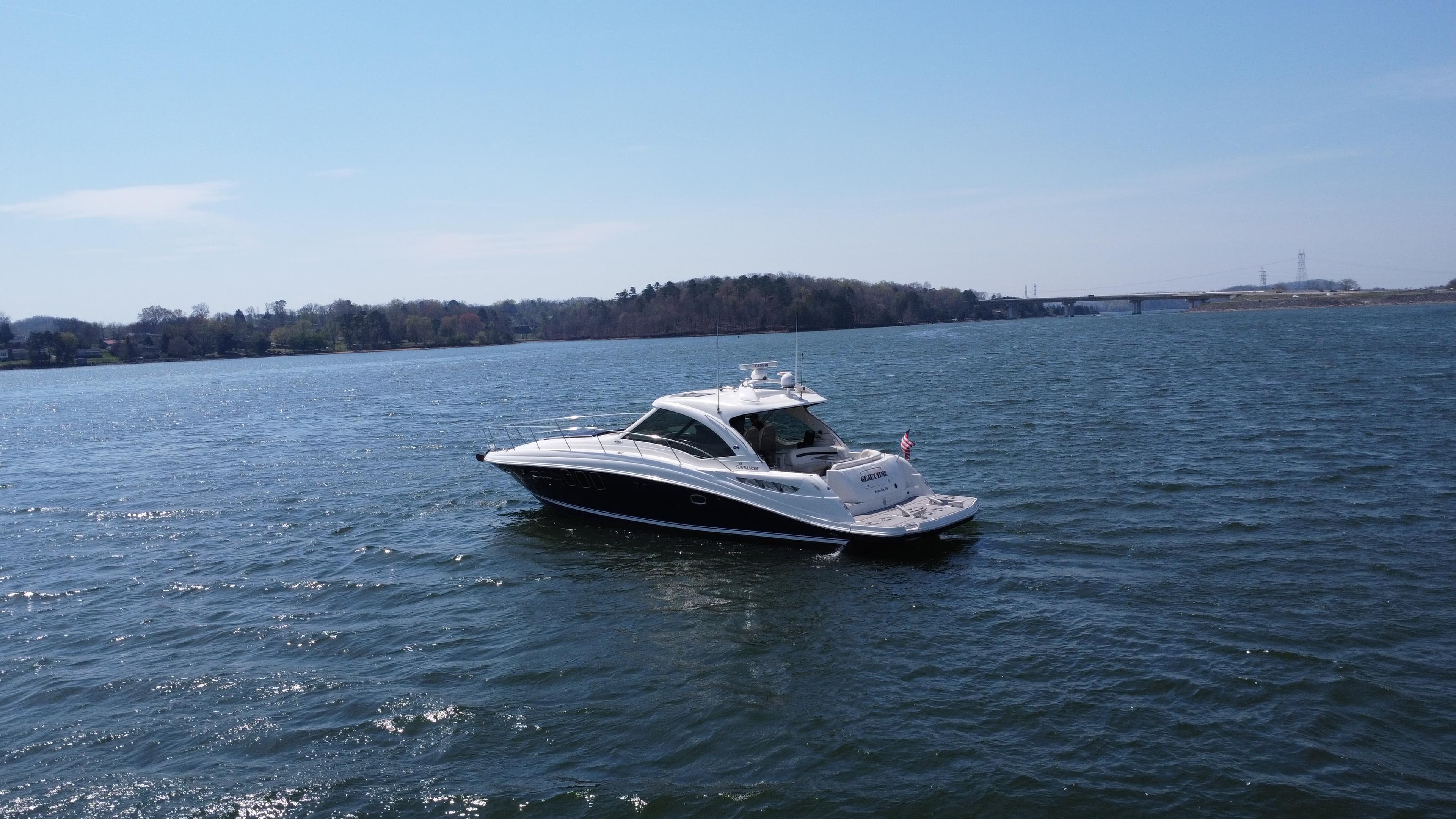 2006 Sea Ray 48 Sundancer yacht cruising on a serene lake under a clear blue sky.