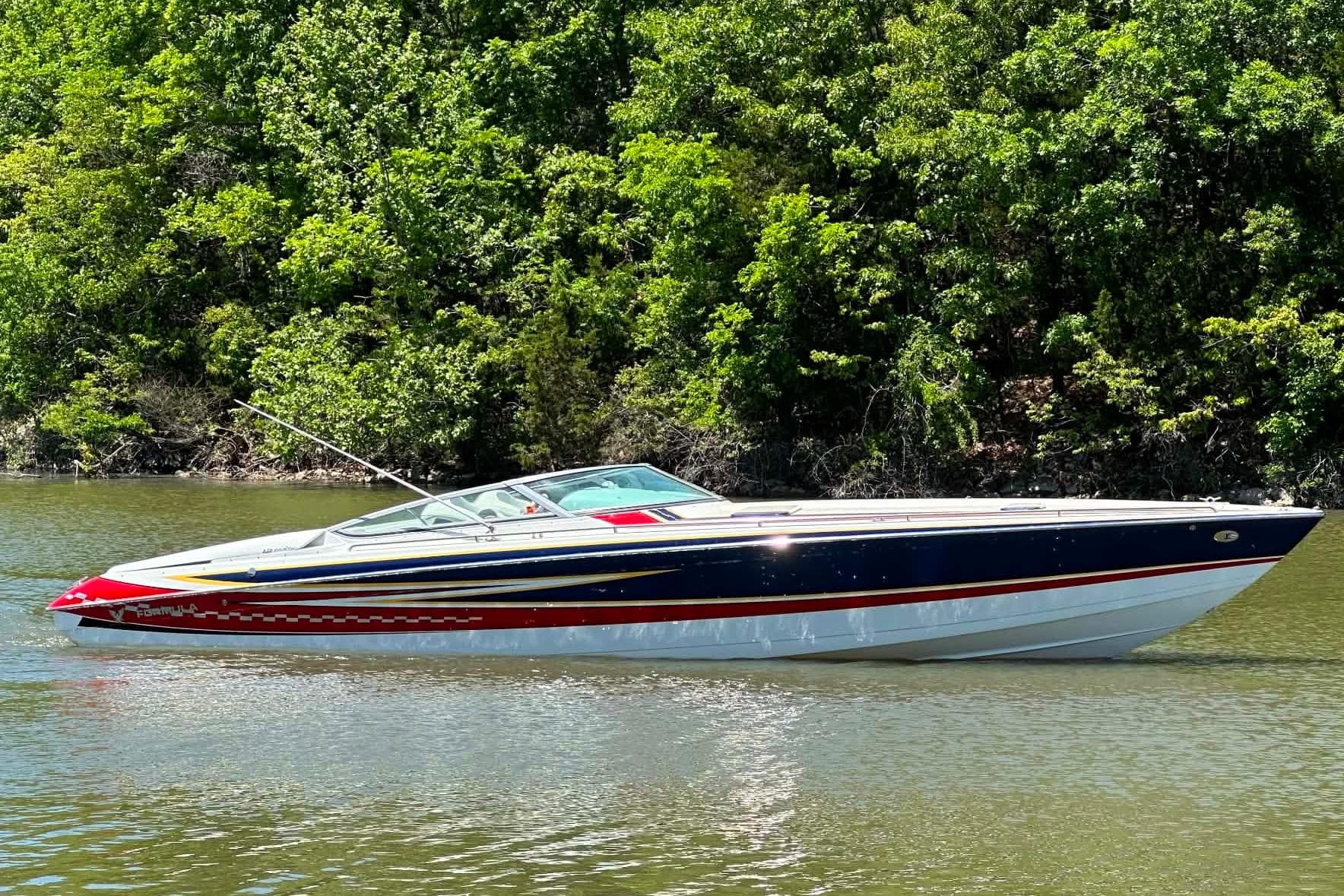 2007 Formula 353 FASTech boat on calm water, surrounded by lush green trees.