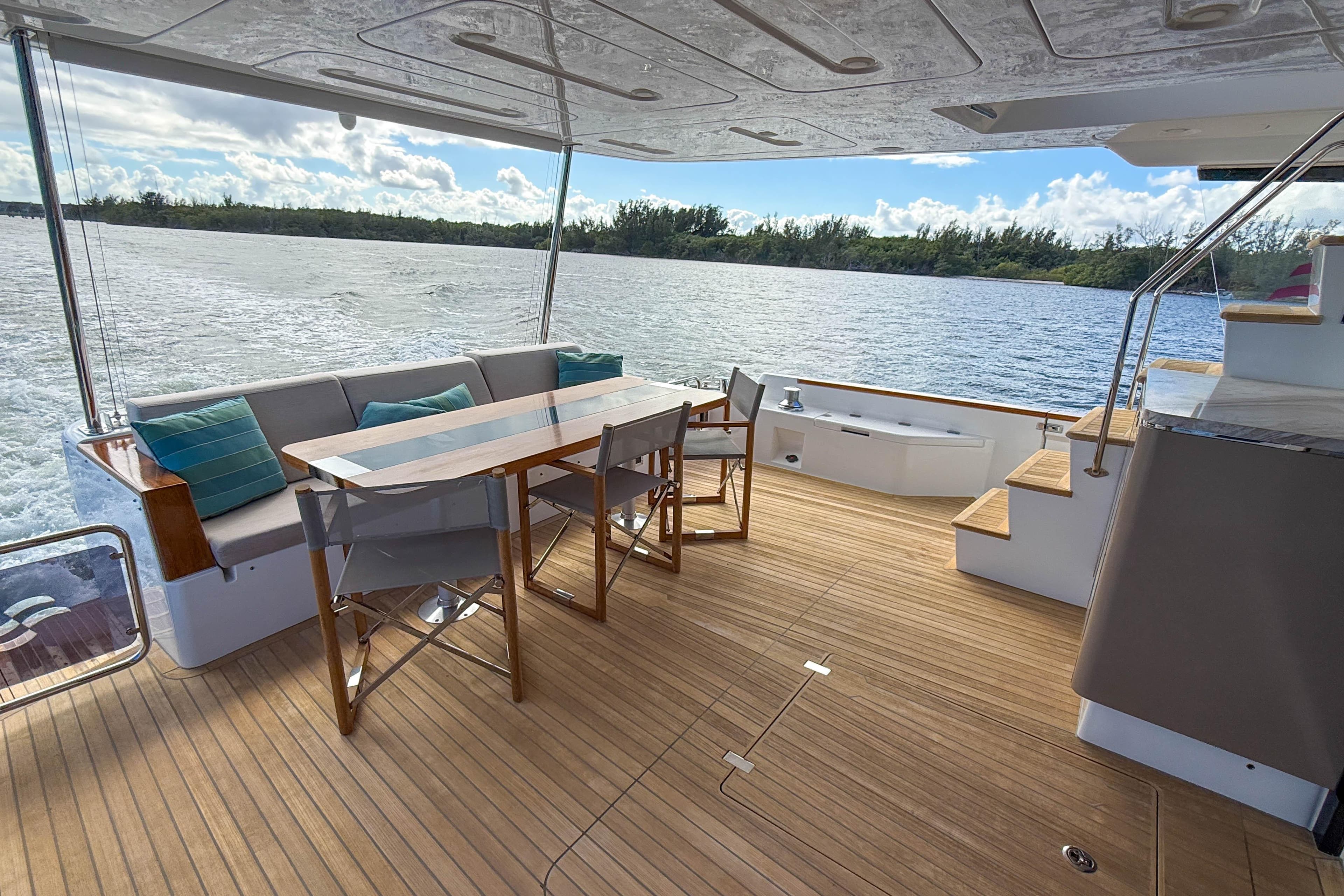 Outdoor seating area on 2023 Sirena 68 yacht with wooden deck and scenic water view.