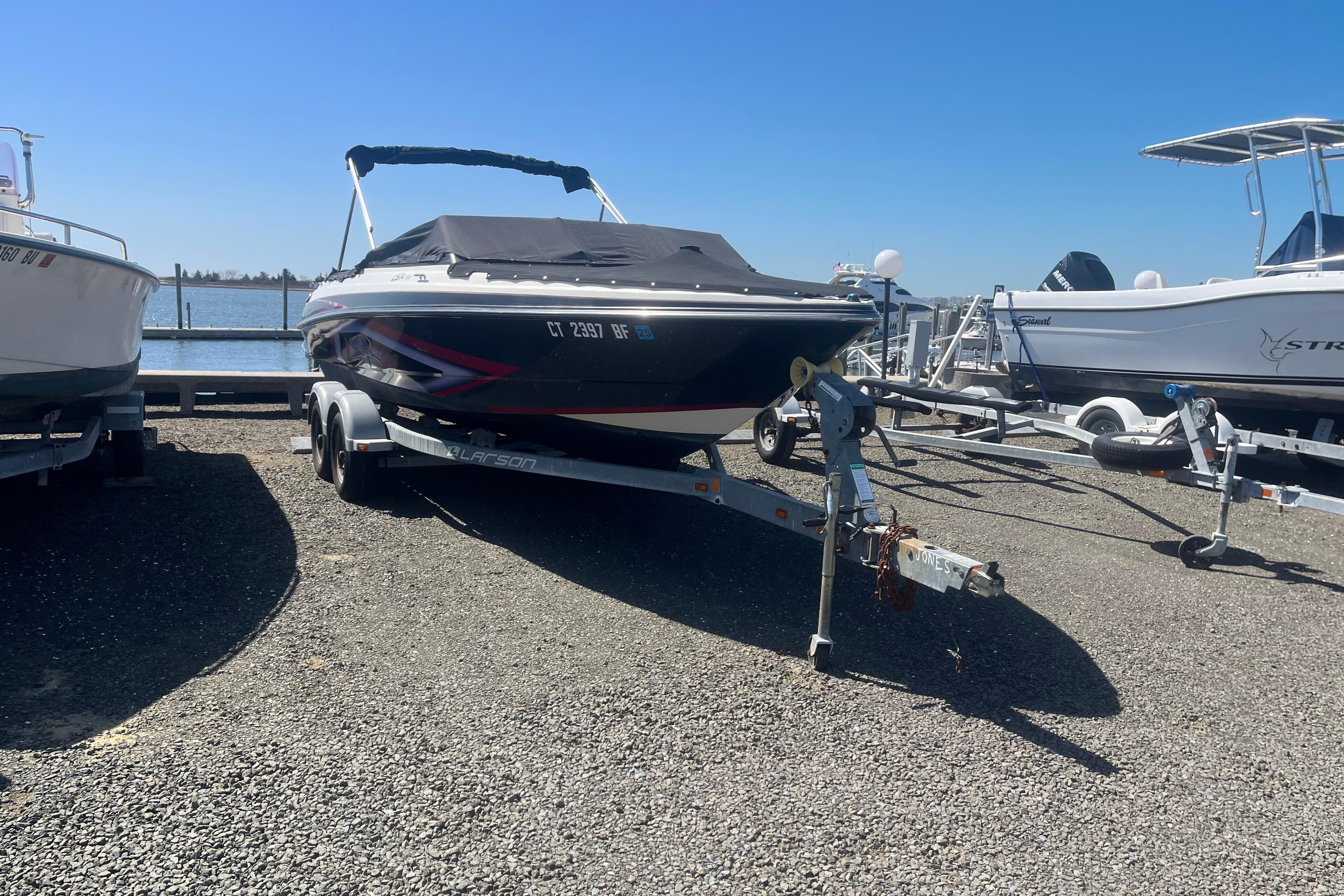 2013 Larson LSR 2300 I/O boat on trailer, parked near waterfront.
