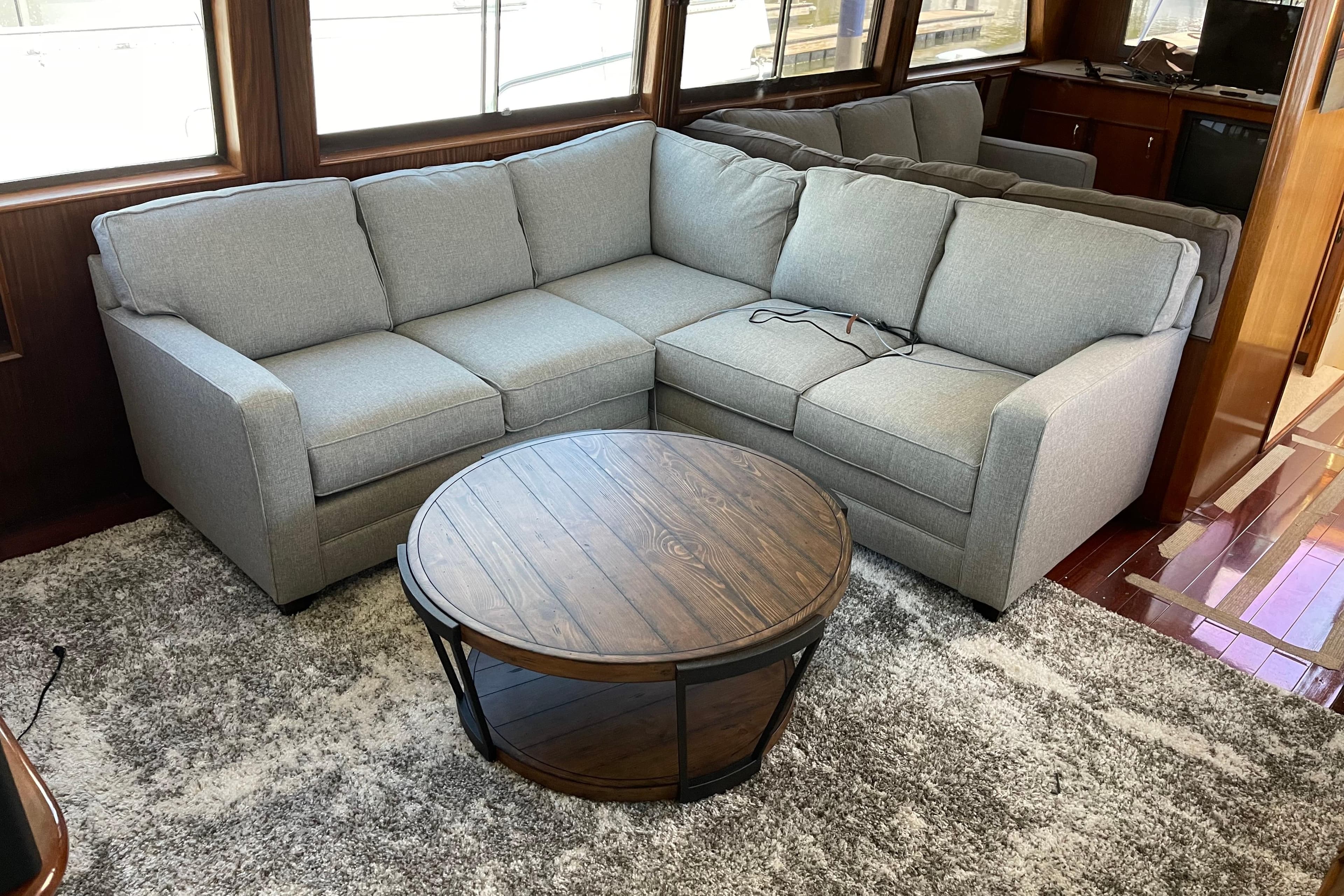 Gray sectional sofa and round wooden table in 1985 Hatteras 60 Convertible yacht interior.