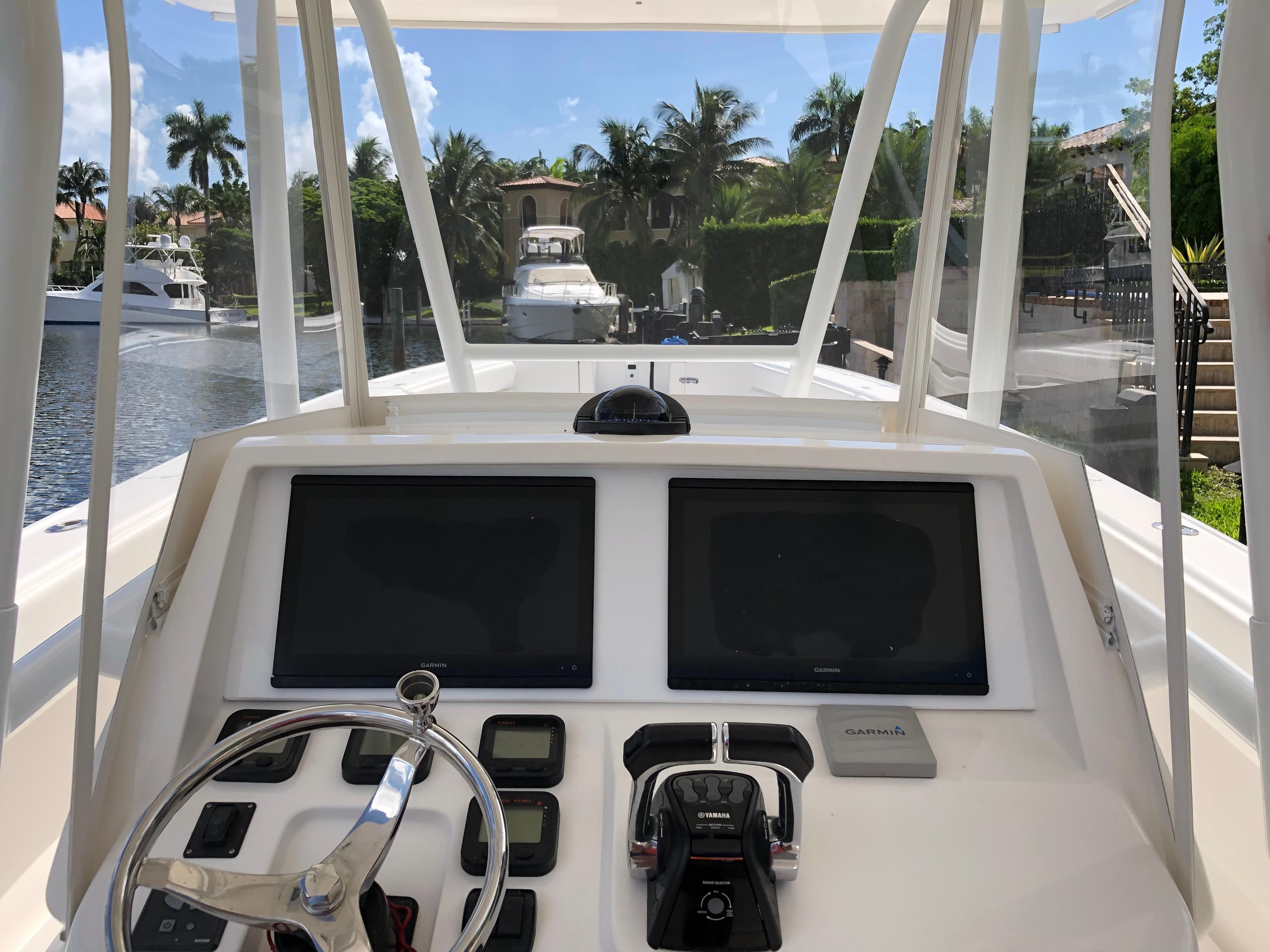 2008 Intrepid 370 boat helm with dual screens and steering wheel, docked near palm trees.