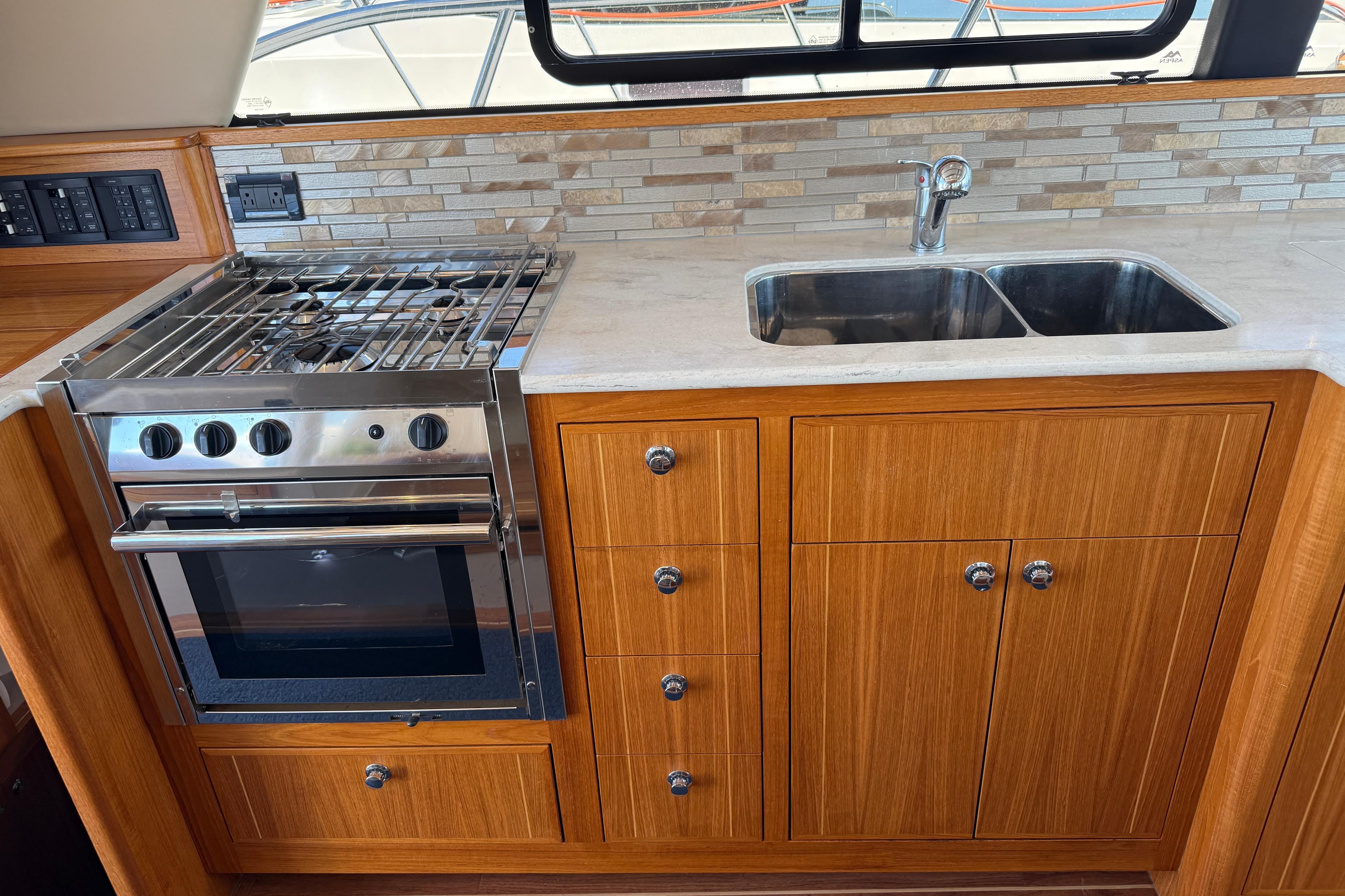 Modern kitchen in 2017 Aspen C120 boat with stove, sink, and wooden cabinetry.