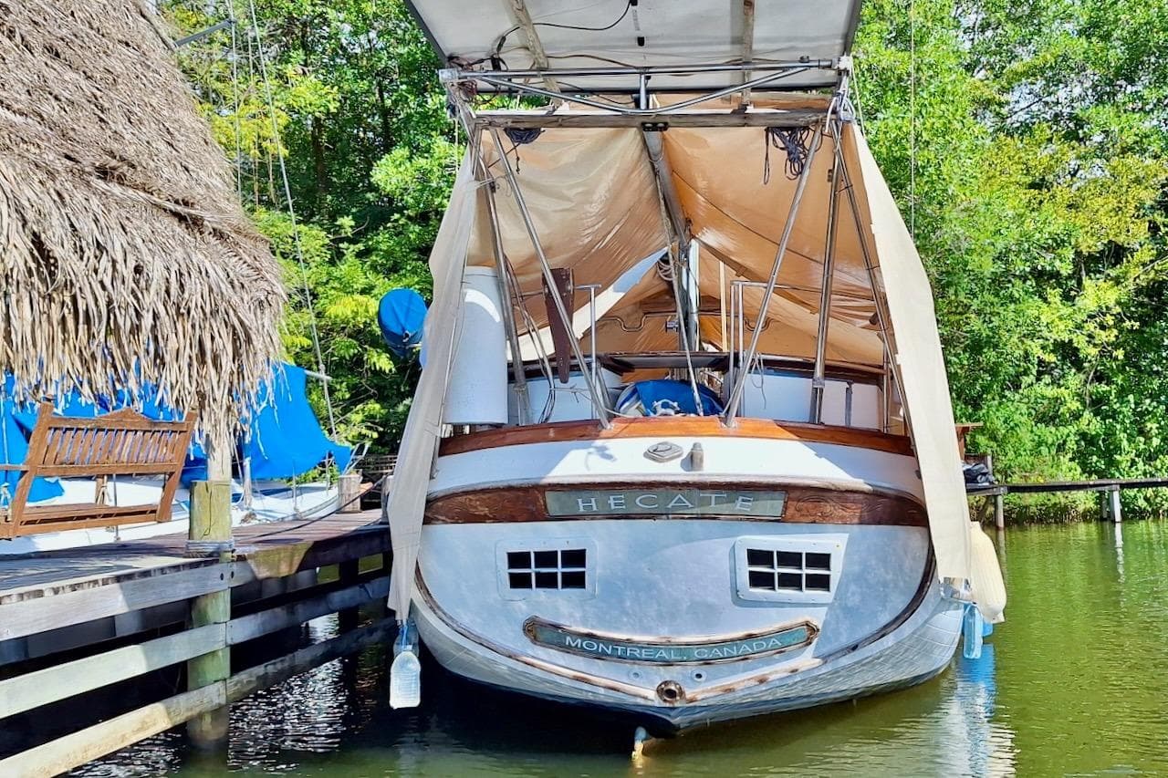 Sailboat Vagabond 47, 1982 model, docked with canopy, lush greenery background.