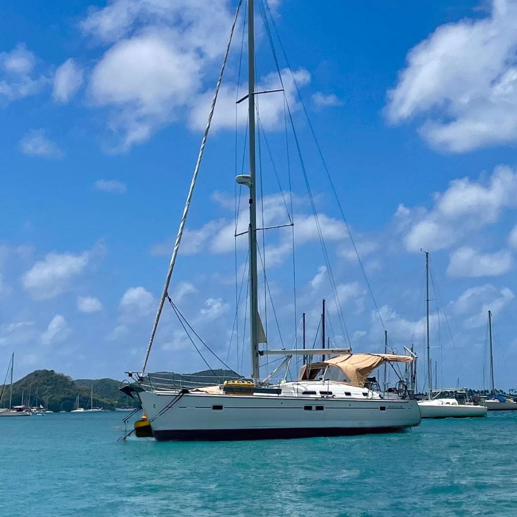 Sailboat Beneteau 423 (2007) anchored in a scenic harbor under a clear blue sky.
