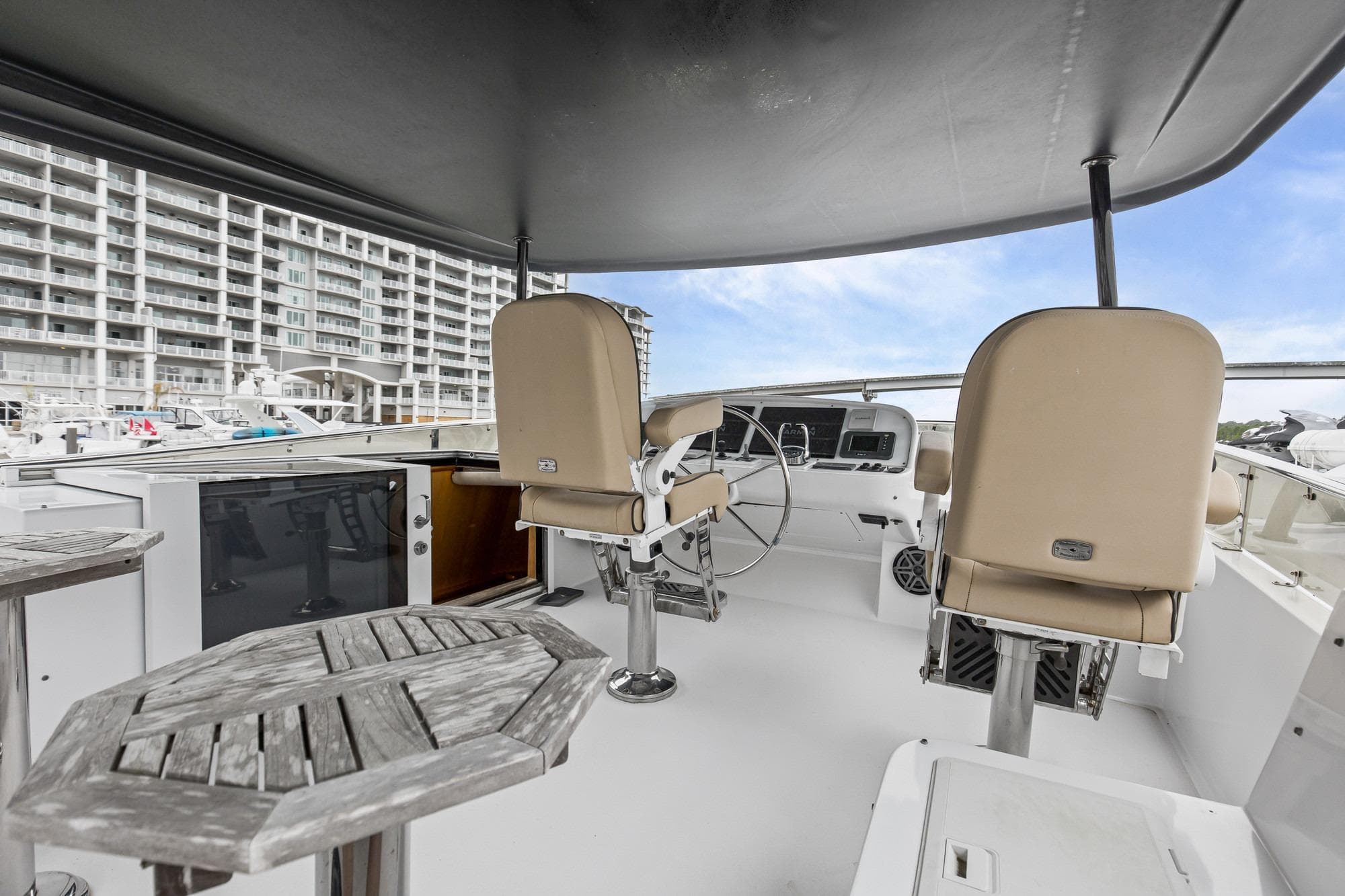 Flybridge of 2004 Queenship 76 Baretta yacht with helm chairs and wooden tables.