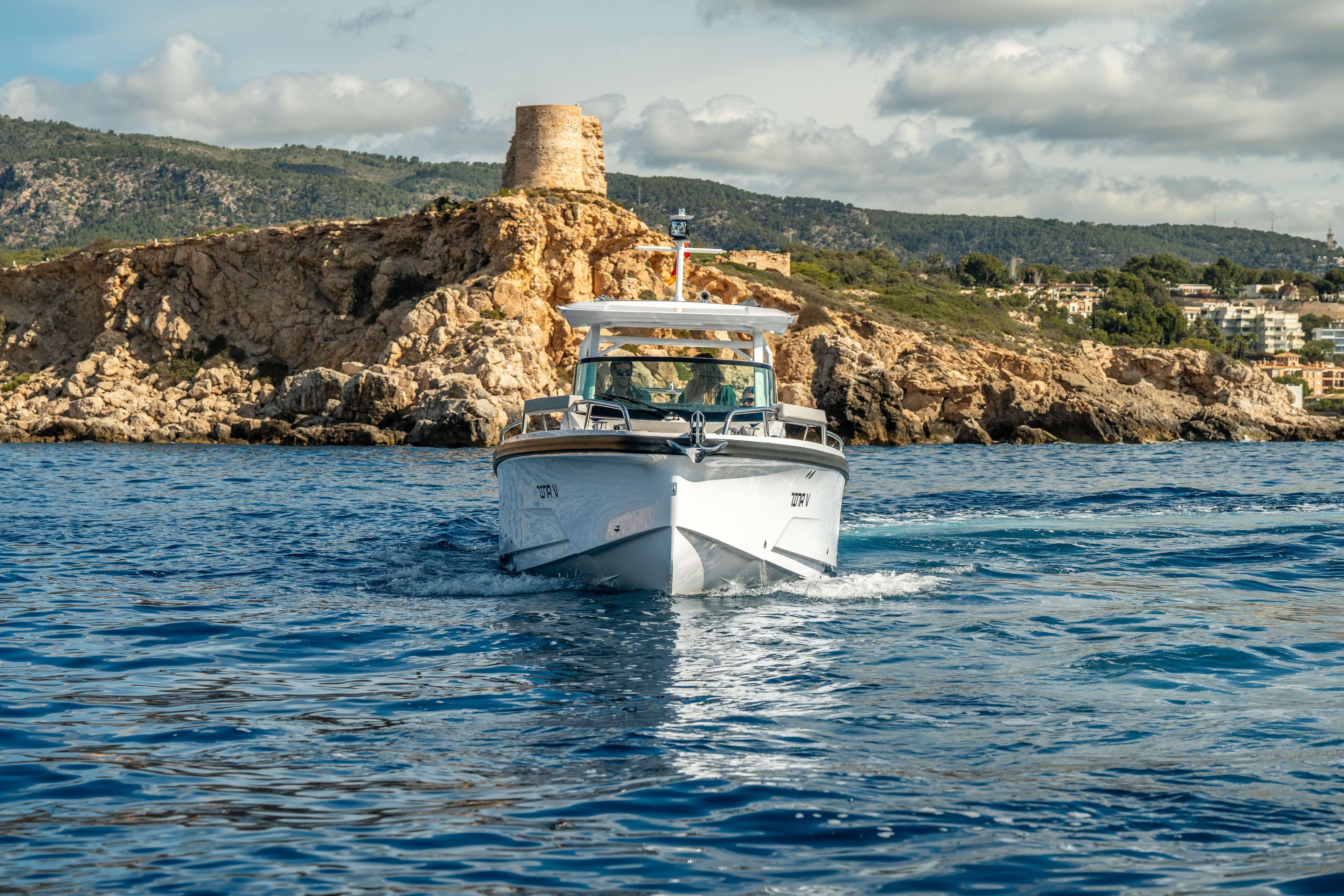 2026 Axopar 29 Sun Top cruising near rocky coastline under a partly cloudy sky.