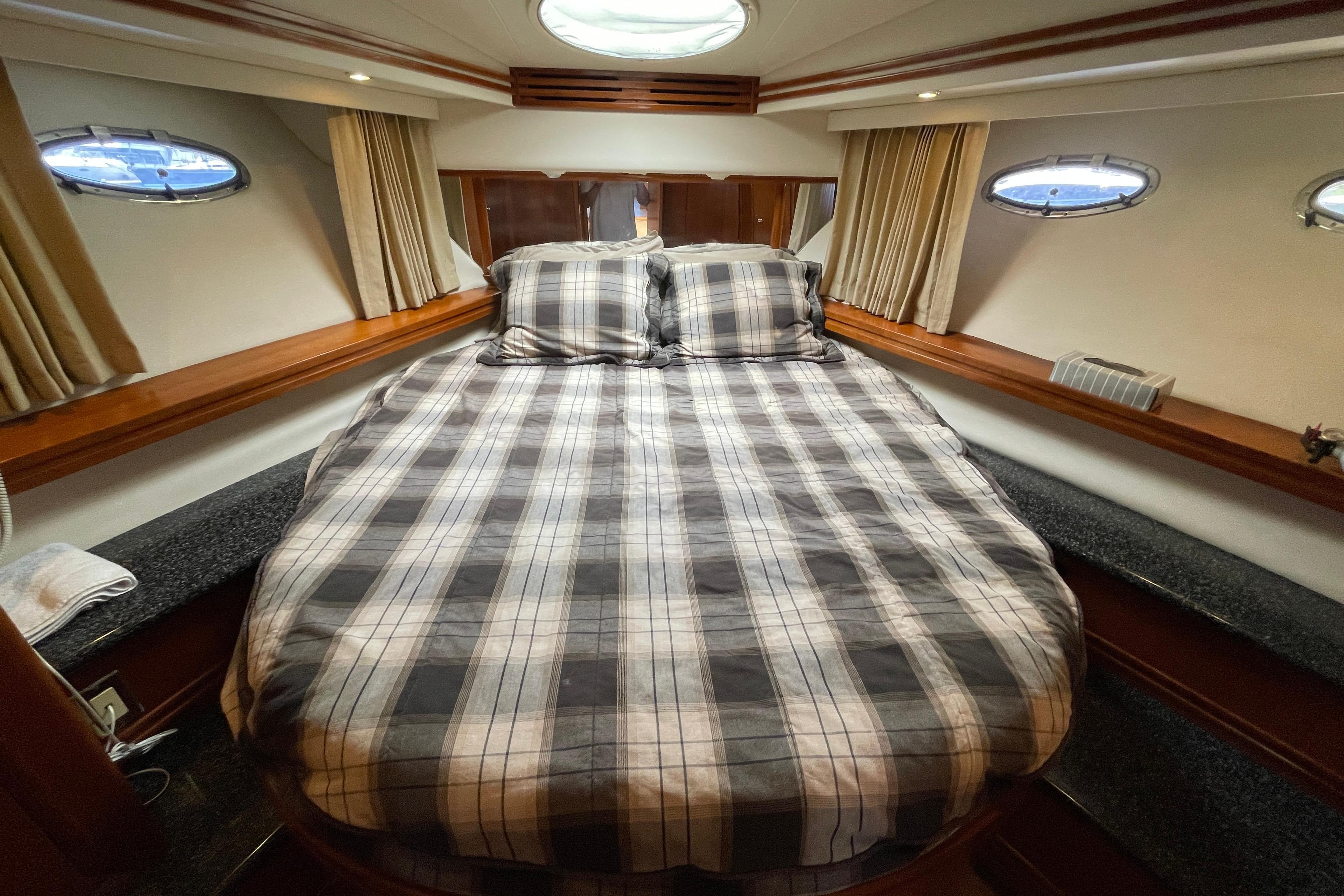 Cozy bedroom in 2000 Carver 506 Motor Yacht with plaid bedding and porthole windows.