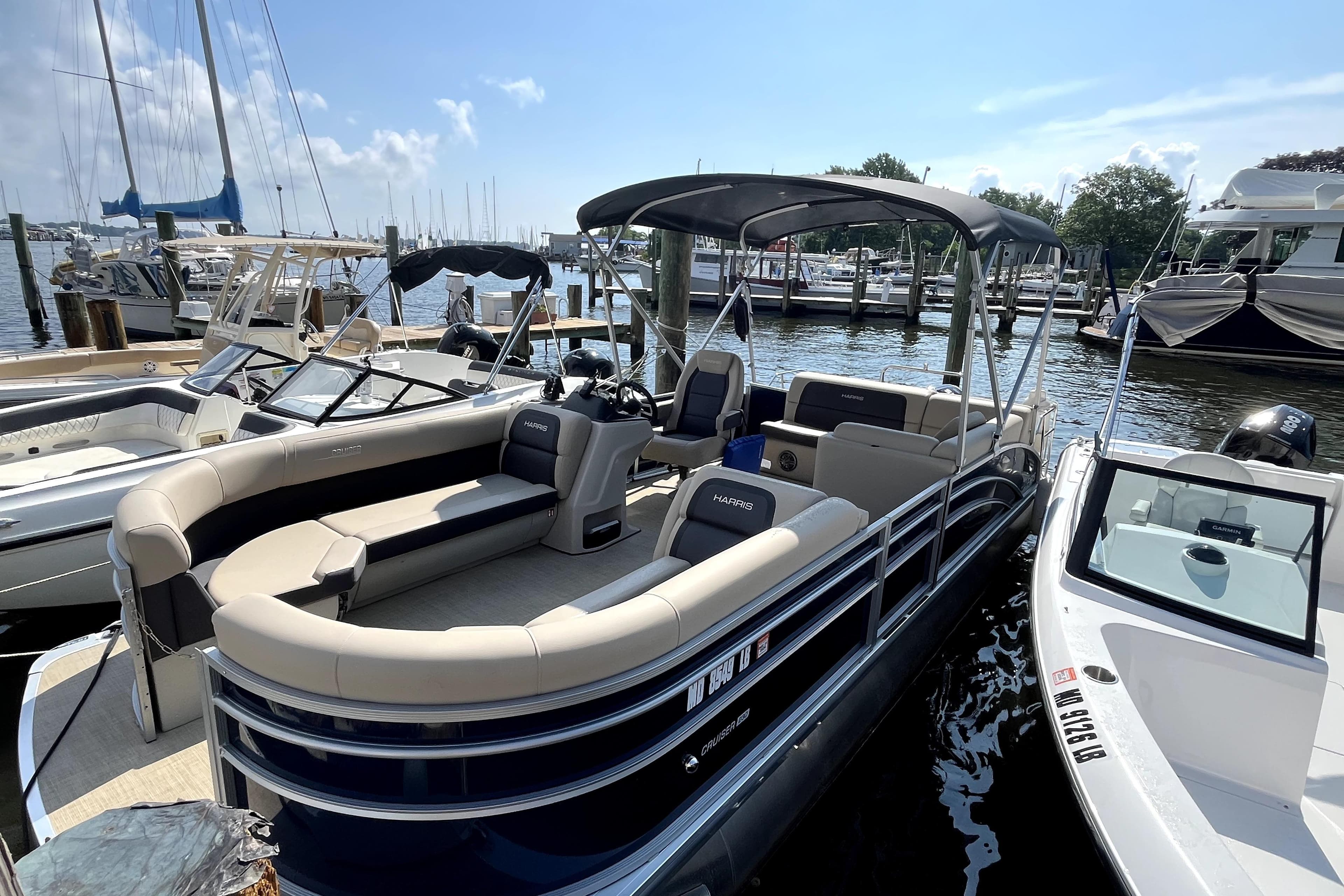2025 Harris HCX23 pontoon boat docked at marina under clear blue sky.