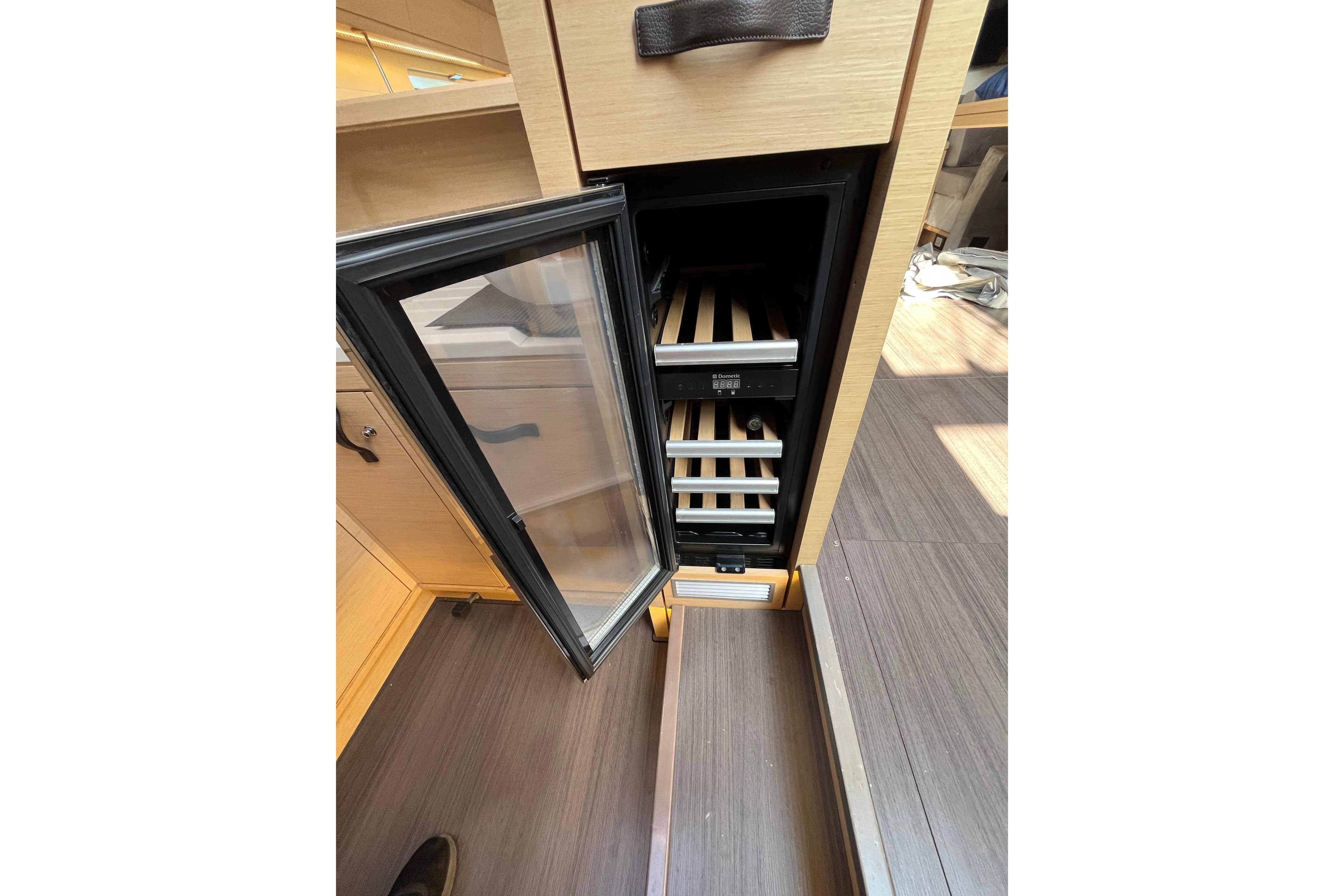 Open wine cooler in 2016 Jeanneau 64 yacht interior, showcasing wooden shelves.
