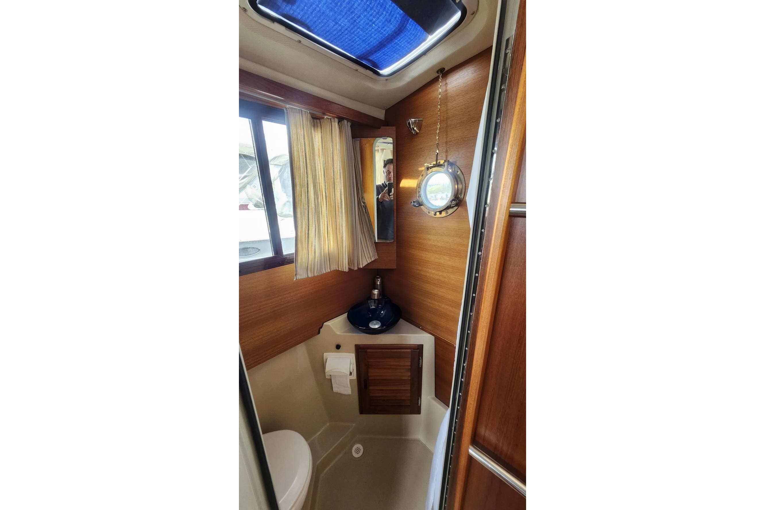 Interior of 2014 Ranger Tugs R-27 boat bathroom with wooden accents and porthole window.