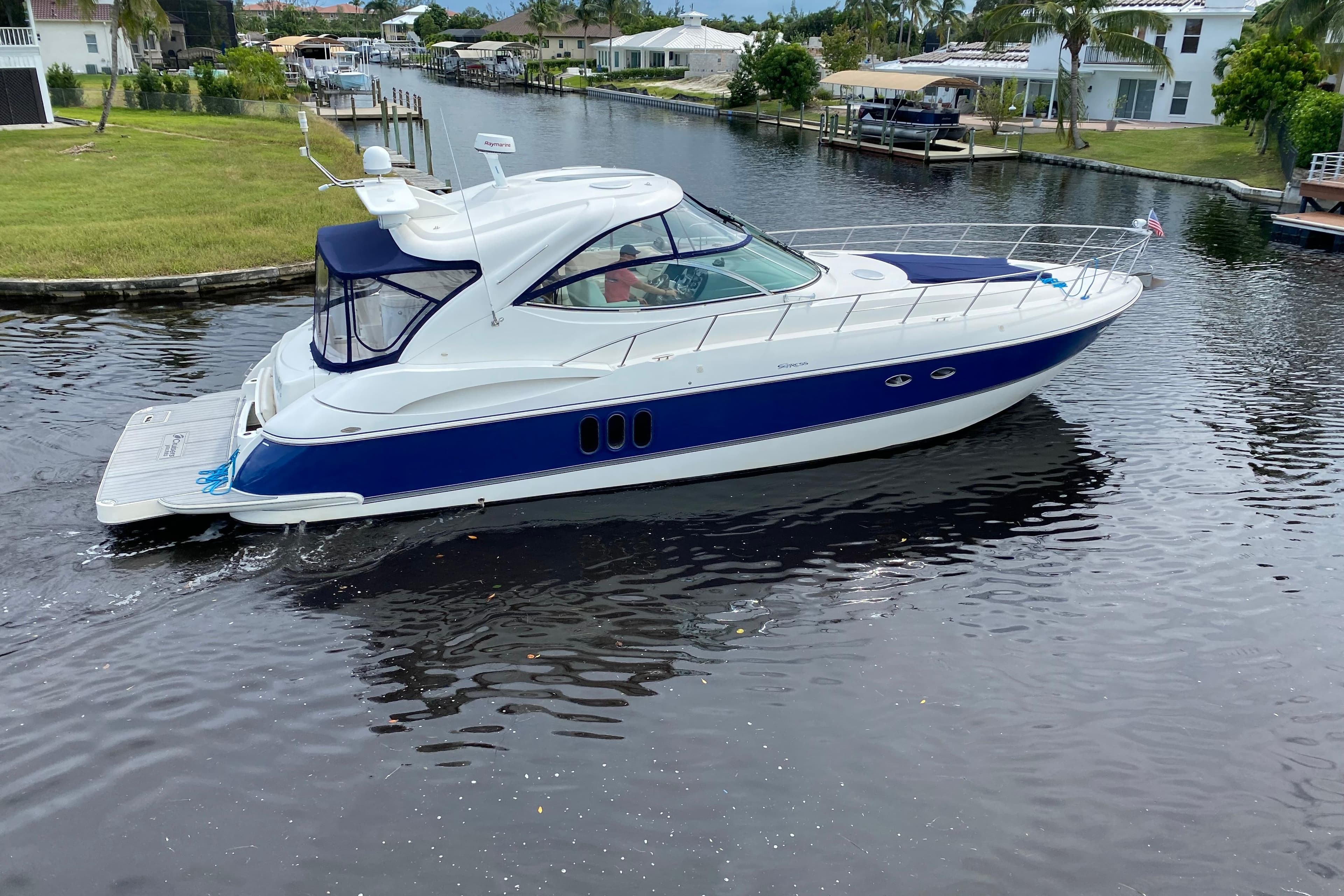 2006 Cruisers Yachts 520 Express navigating a serene canal, surrounded by lush greenery.