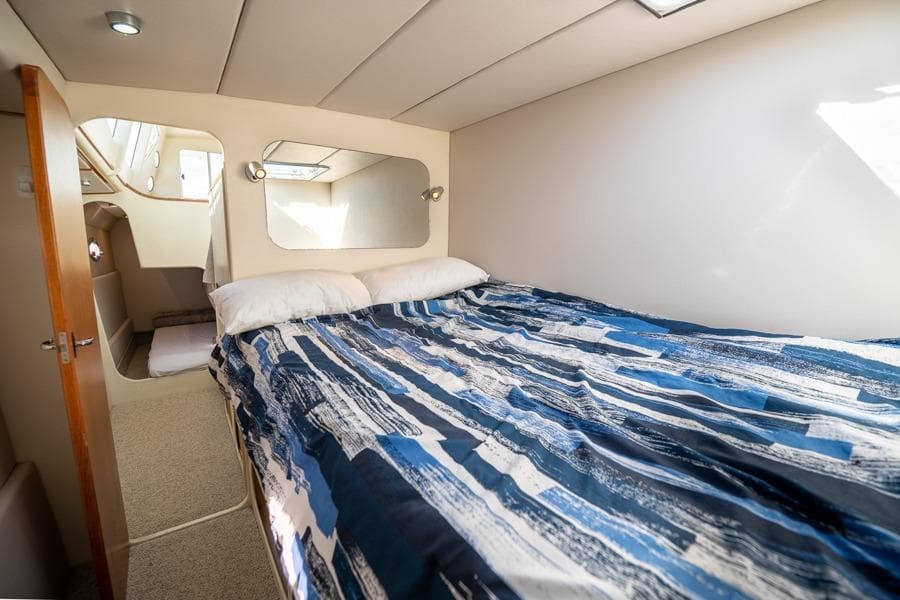 1991 Ron Given Power Catamaran cabin with bed, mirrors, and blue bedding.