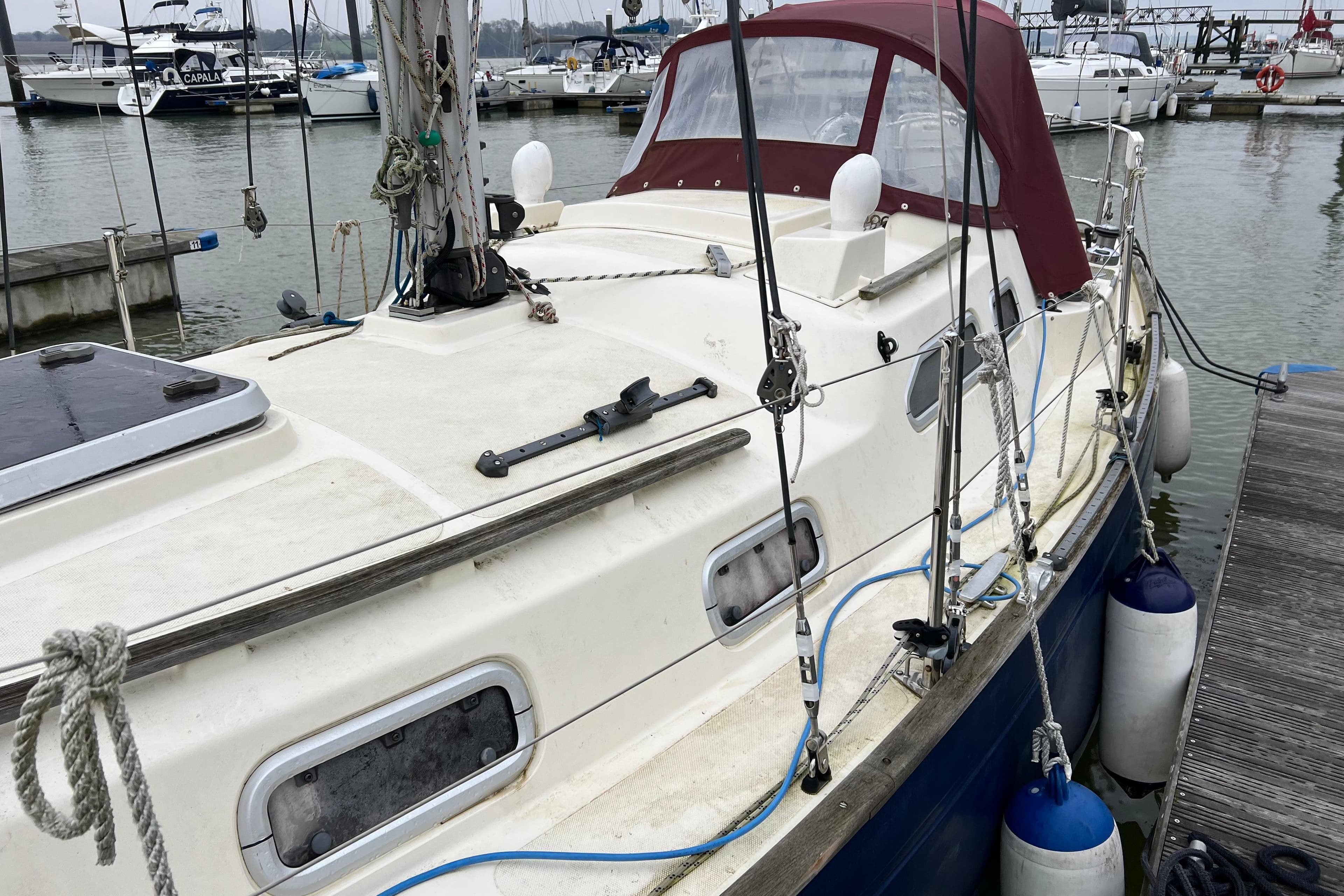 Sailboat docked at marina, Vancouver 28 model, featuring a maroon canopy and nautical equipment.