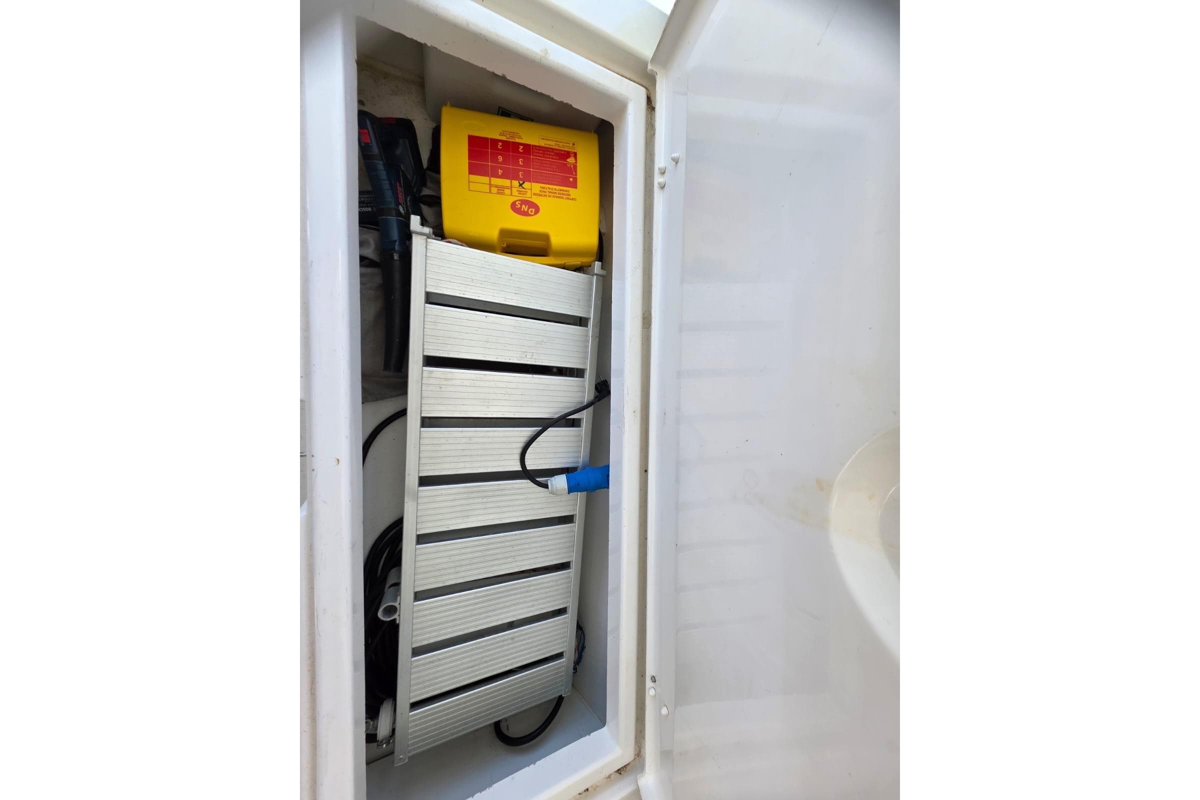 Storage compartment in a 2016 Bali 4.5 boat, featuring a yellow battery and equipment.