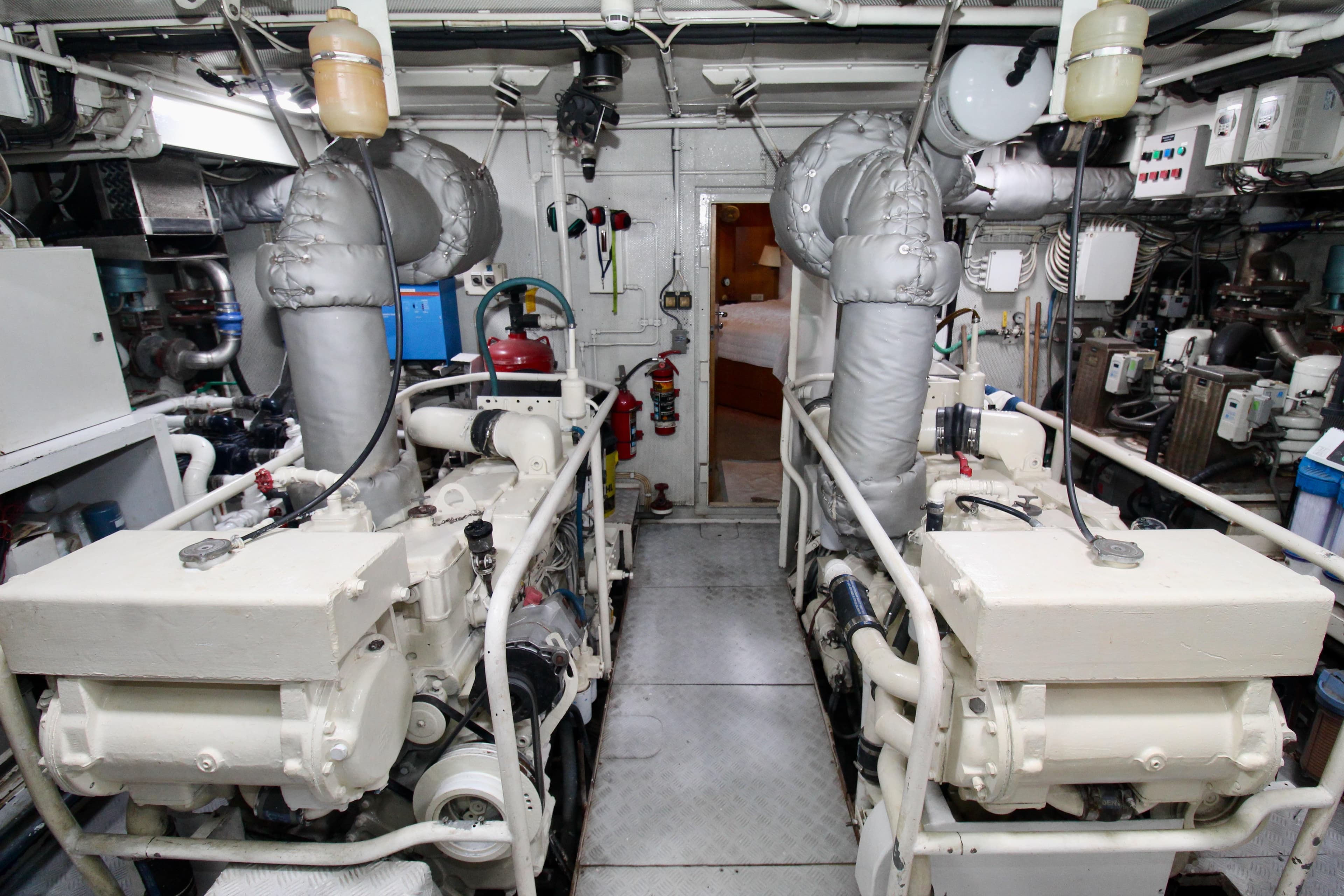 Engine room of a 1990 Hakvoort Motor Yacht, featuring dual engines and complex piping.