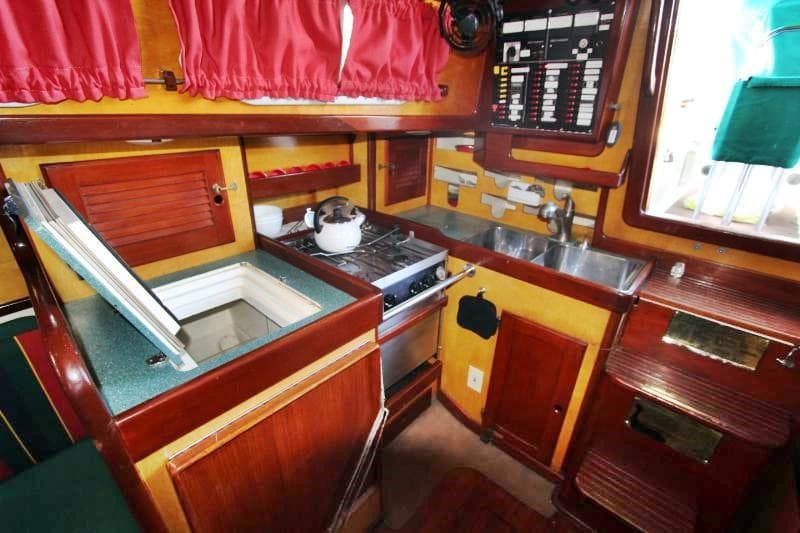 1978 Bristol 40 yacht kitchen with stove, sink, and red curtains.