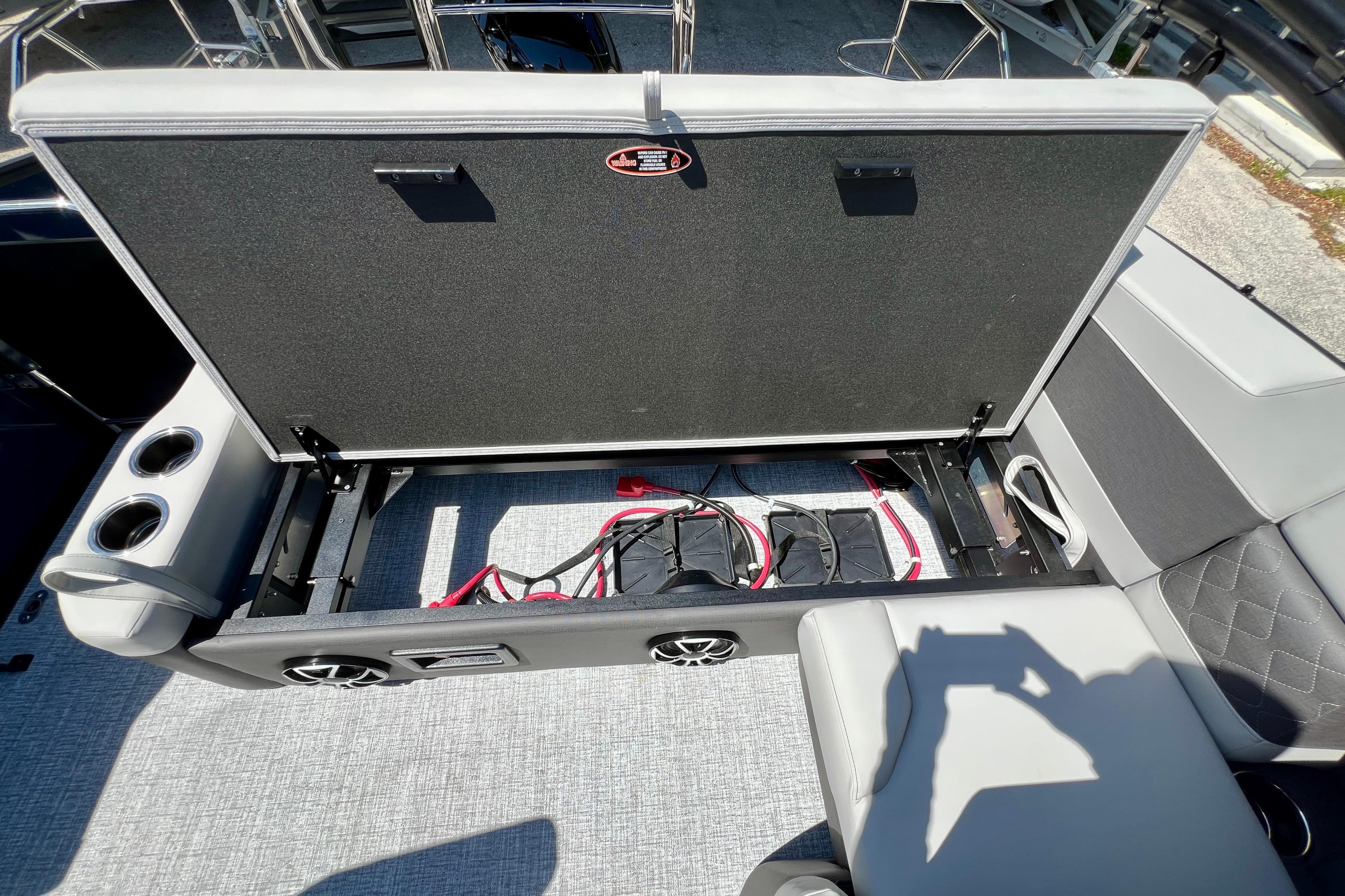 Open storage compartment on 2026 Harris Sunliner 210 boat, featuring cup holders and speakers.