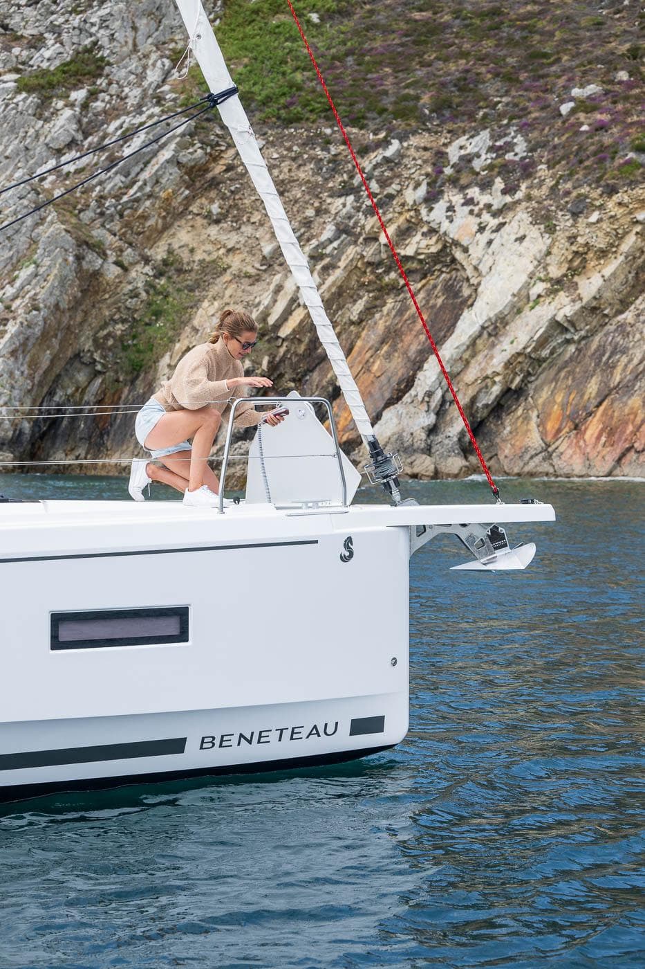 Woman on 2026 Beneteau Oceanis 37.1 yacht near rocky coastline.